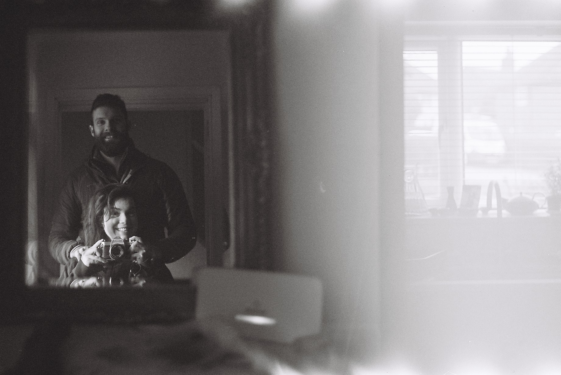 A photo of a mirror in which is the reflection of two people operating a single camera; the right side of the frame is whited-out, probably because one of those people accidentally opened the camera while the film was still exposed