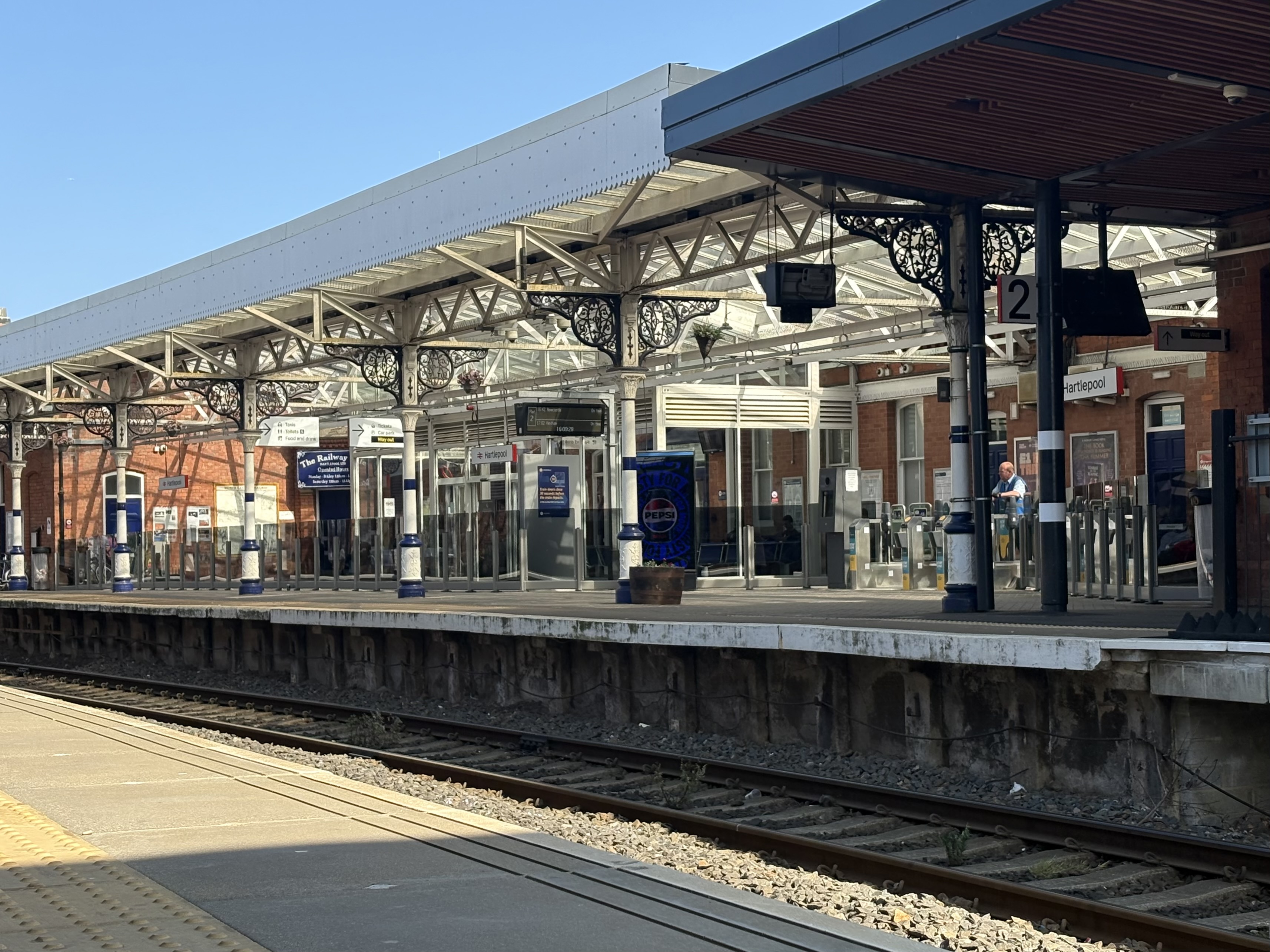 Hartlepool station platform, covered with wrought iron and with a man standing by the turnstiles in the corner