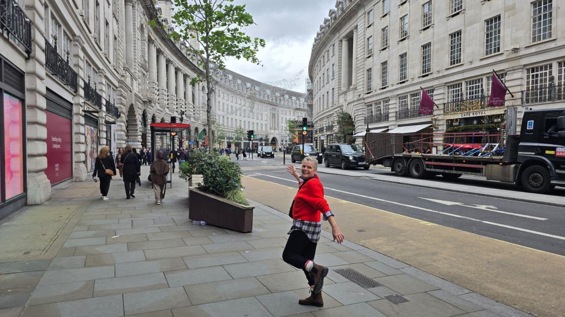 A woman in a red sweater walking down a curved street in London, with tall white buildings lining the road on either side and expensive shops on the ground floors