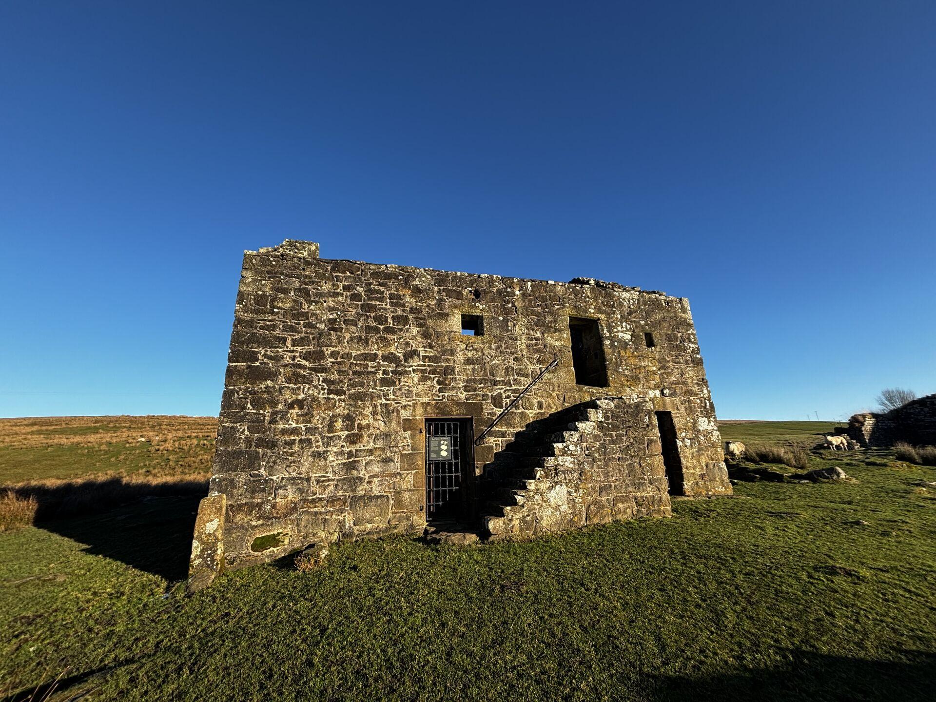 A fortified stone farmhouse used in the Tudor period, standing in a green grassy field