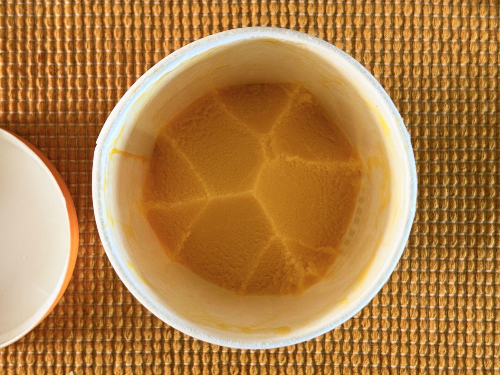 Looking down into a half-eaten cup of mango sorbet on a yellow placemat.