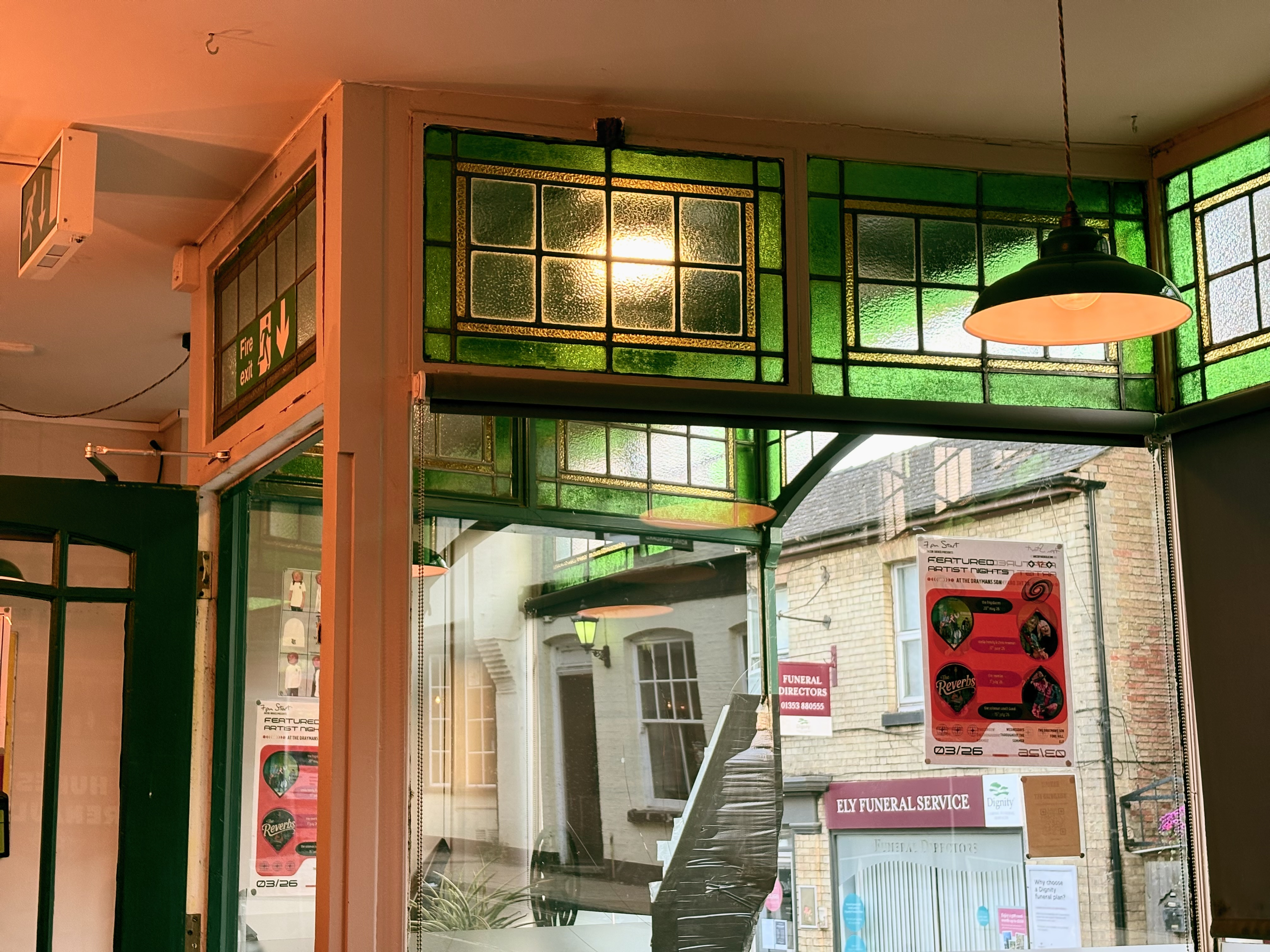 Looking out the stained glass windows of the Drayman’s Son, some posters on the windows and the street beyond.