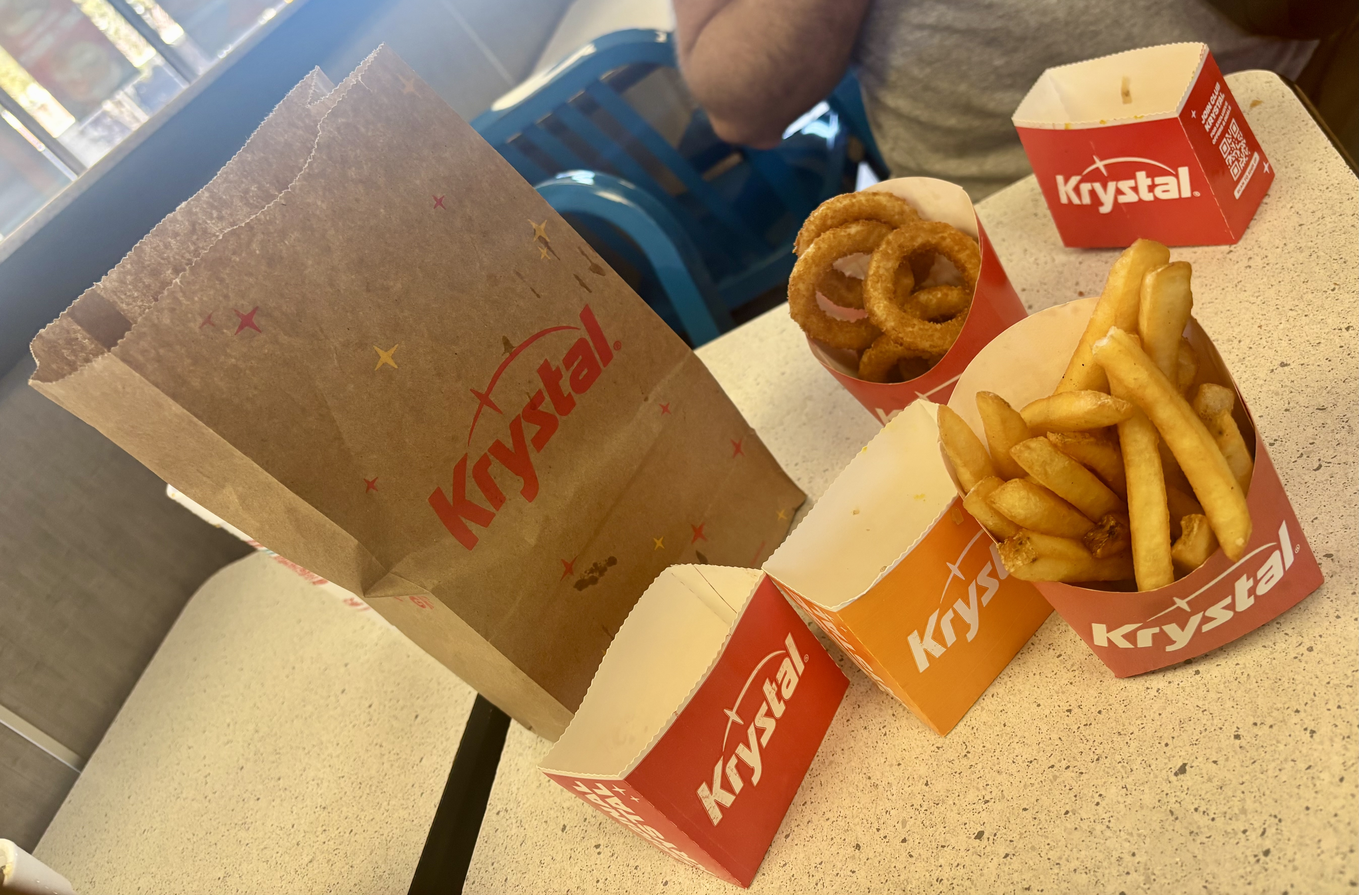 Some fast food fries and onion rings on a table next to a paper bag.