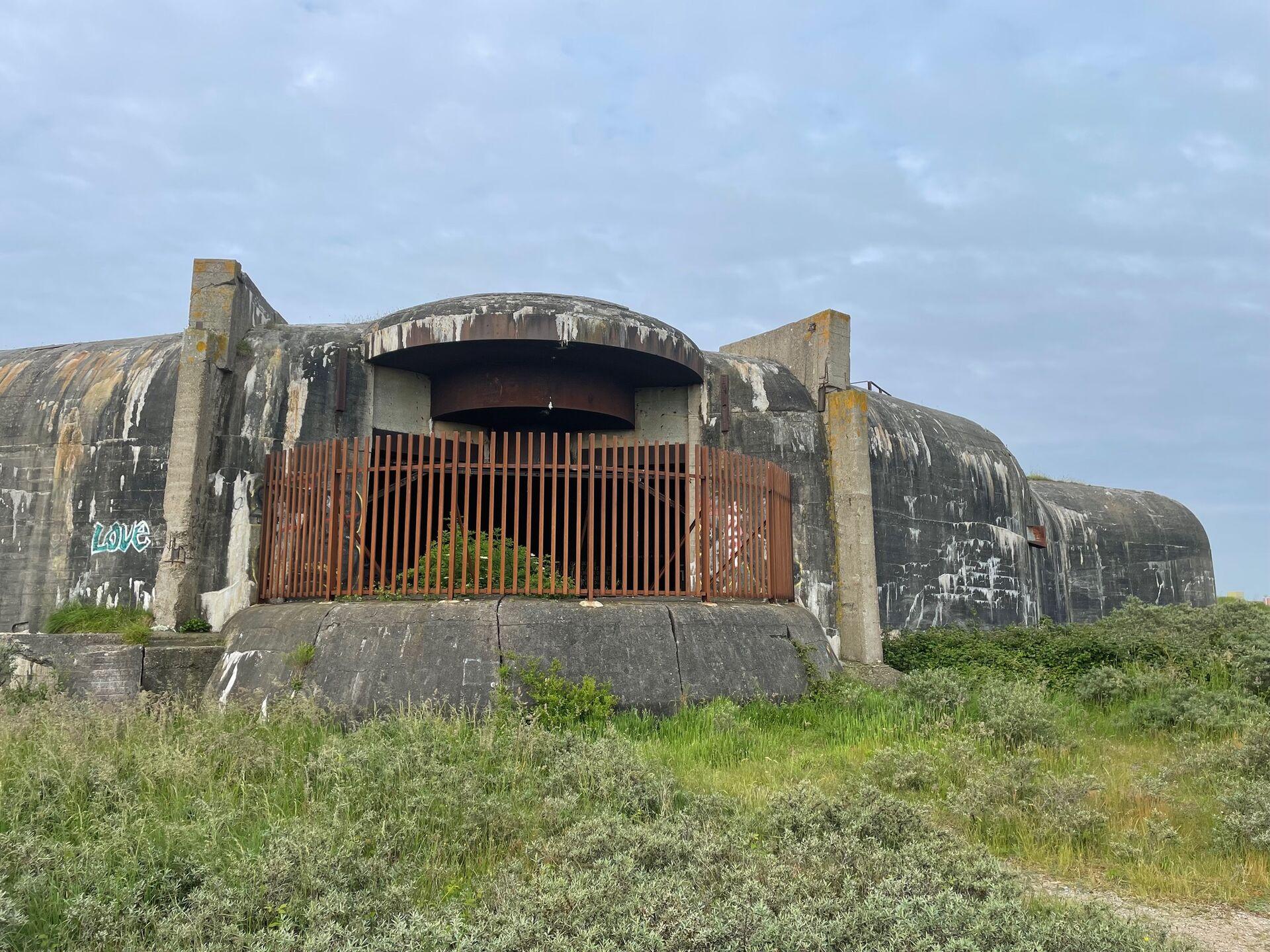 A massive concrete artillery bunker, with the gun portal blocked up by a rusty fence