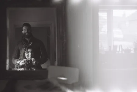 A photo of a mirror in which is the reflection of two people operating a single camera; the right side of the frame is whited-out, probably because one of those people accidentally opened the camera while the film was still exposed