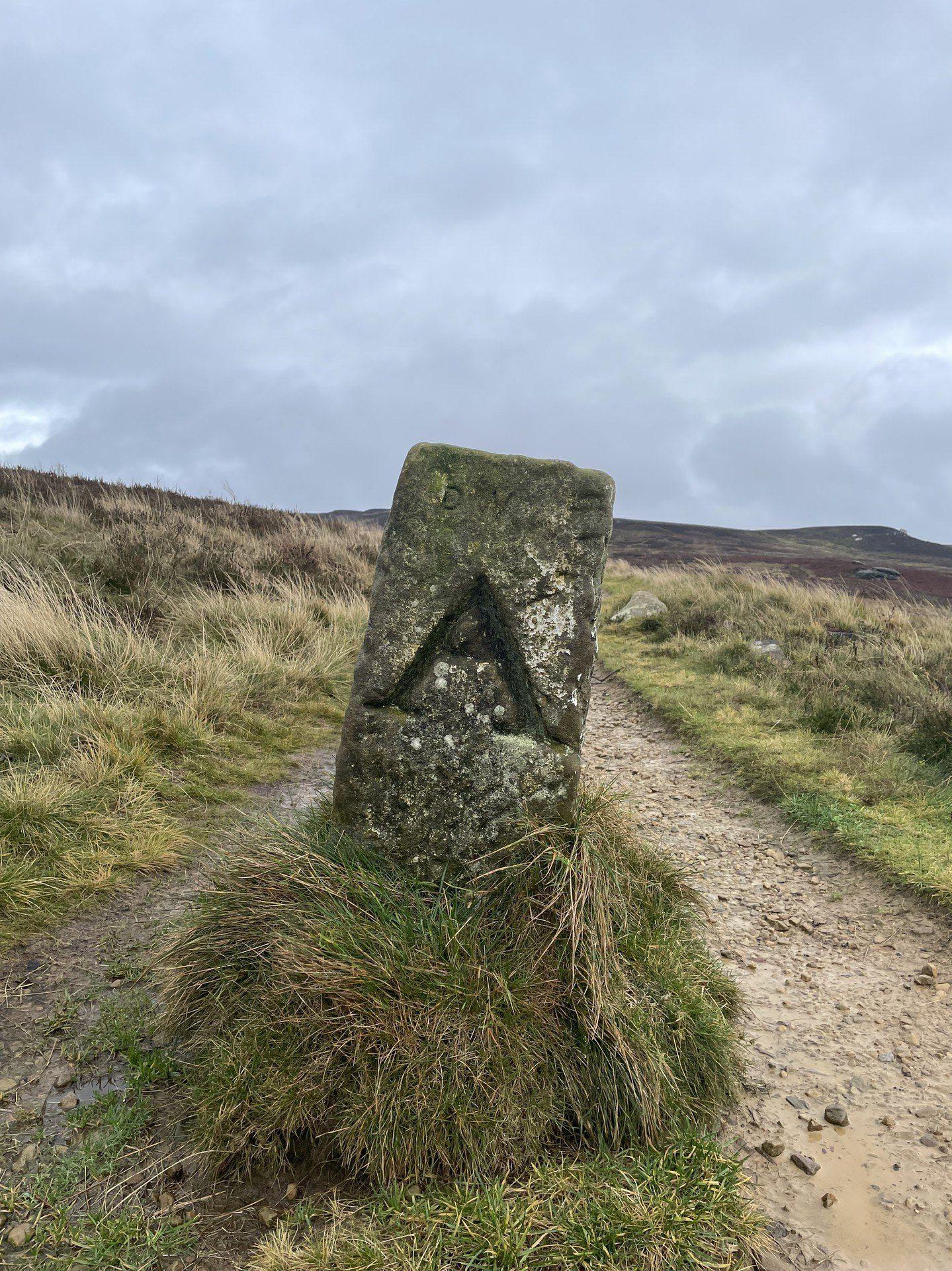 An old boundary stone with the letter A carved into it, plumb in the middle of the path.