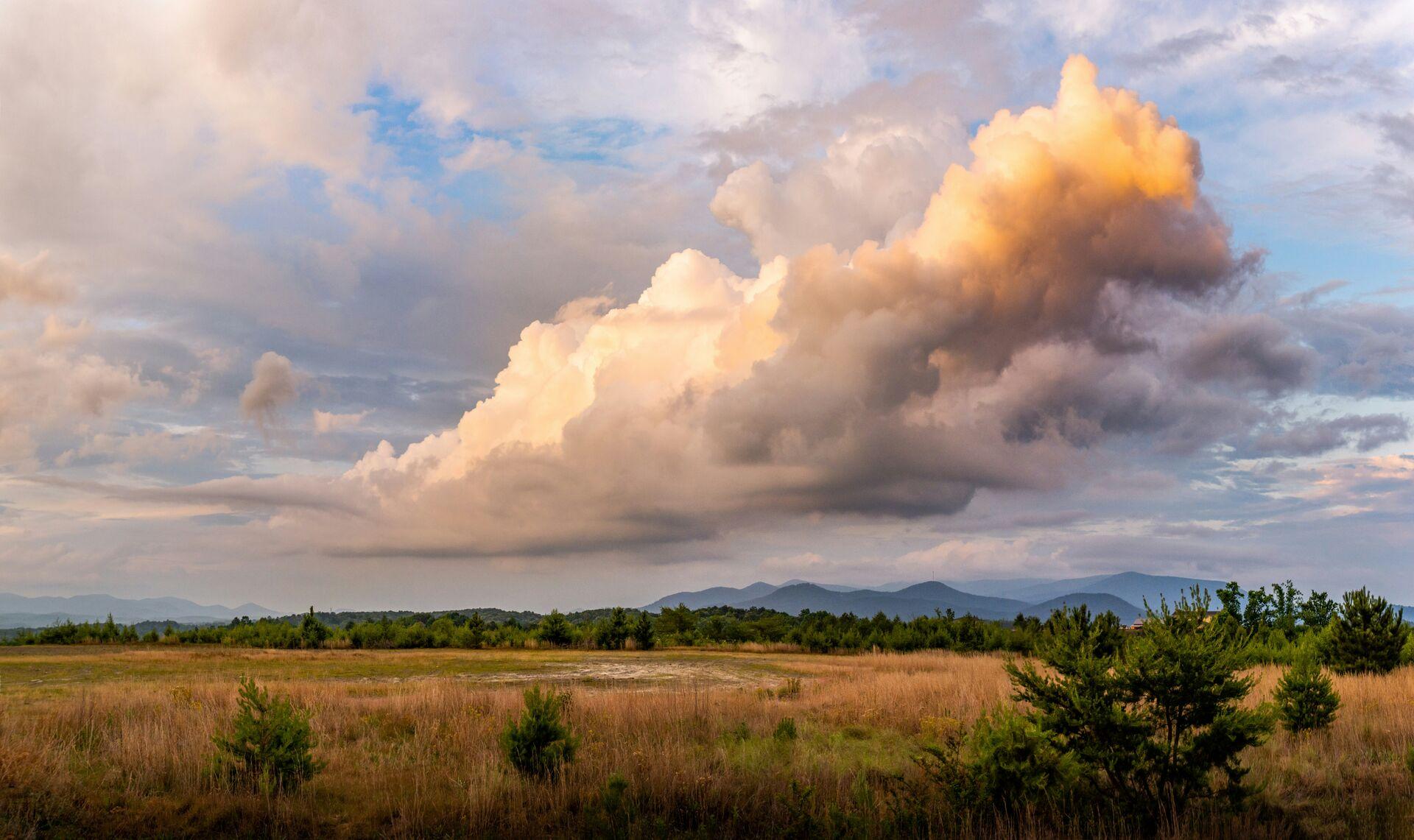 Fluffy looking orange clouds at sunset, over an auburn field of grass and with dark hills rising in the far distance