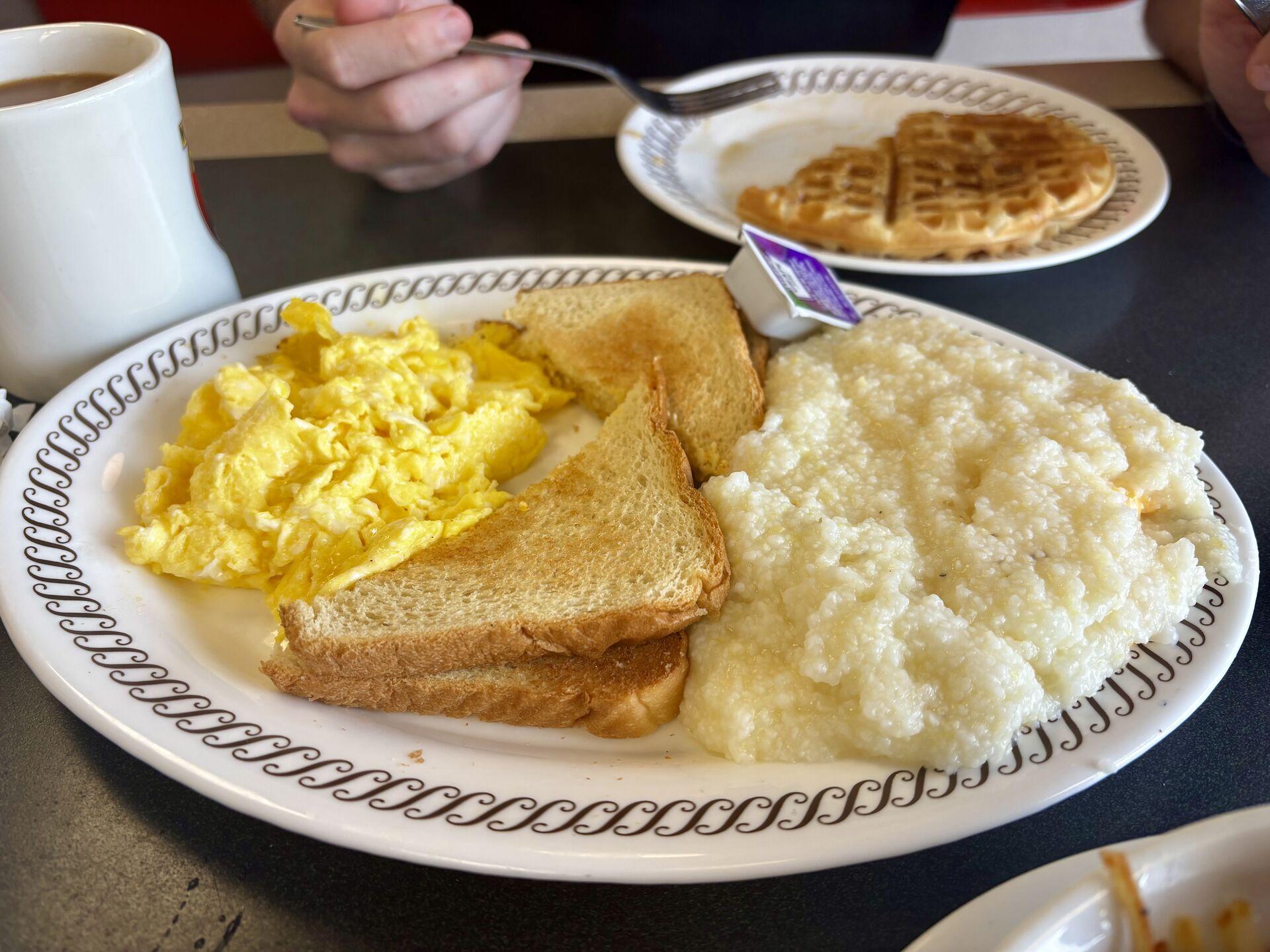 A plate of scrambled eggs, white toast, and a heaping portion of corn grits