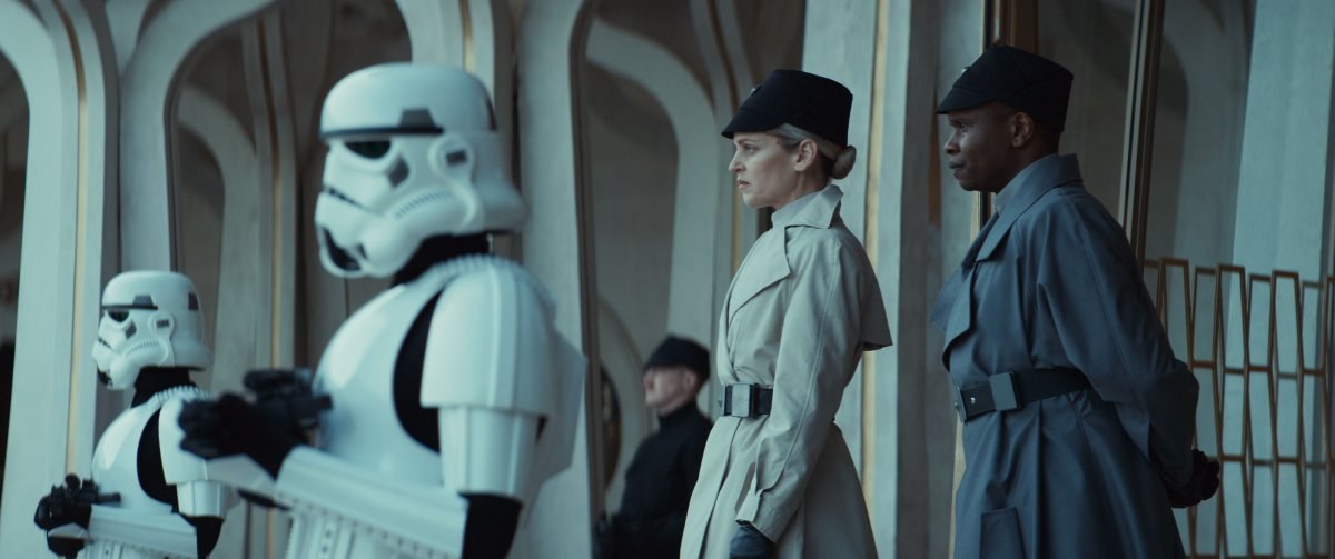 A scene from Andor, showing two Empire officers in uniform standing behind two Stormtroopers under a white sculpted colonnade