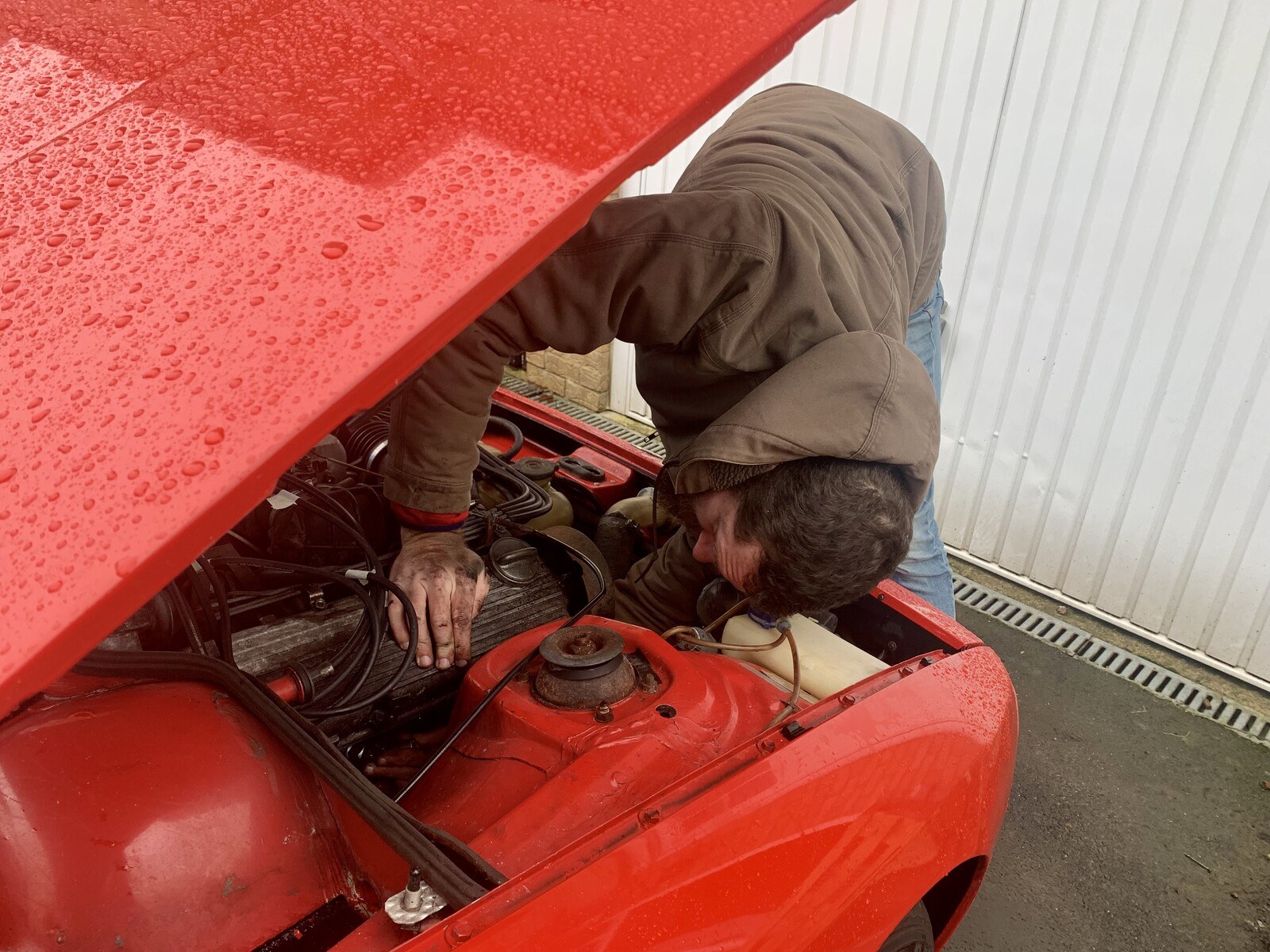 Me, bending over the engine bay of a red Porsche 924, with my hand reaching wayyy back underneath the engine for spark plug number 4