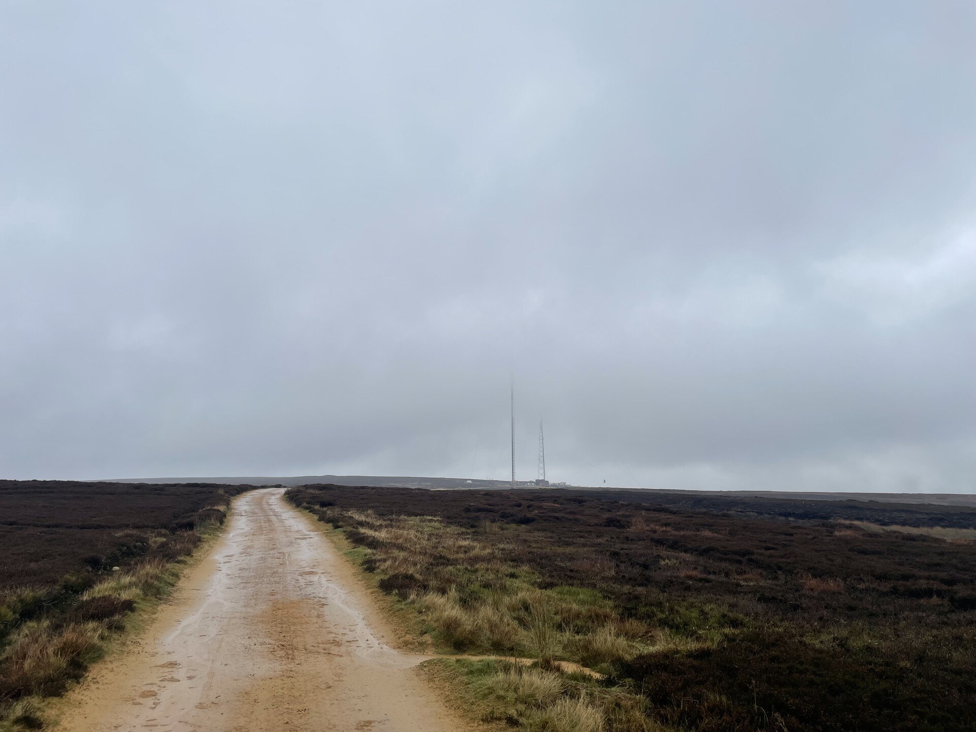 A dirt track stretching off across Bilsdale West moor, with the transmitting tower in the clouds in the distance