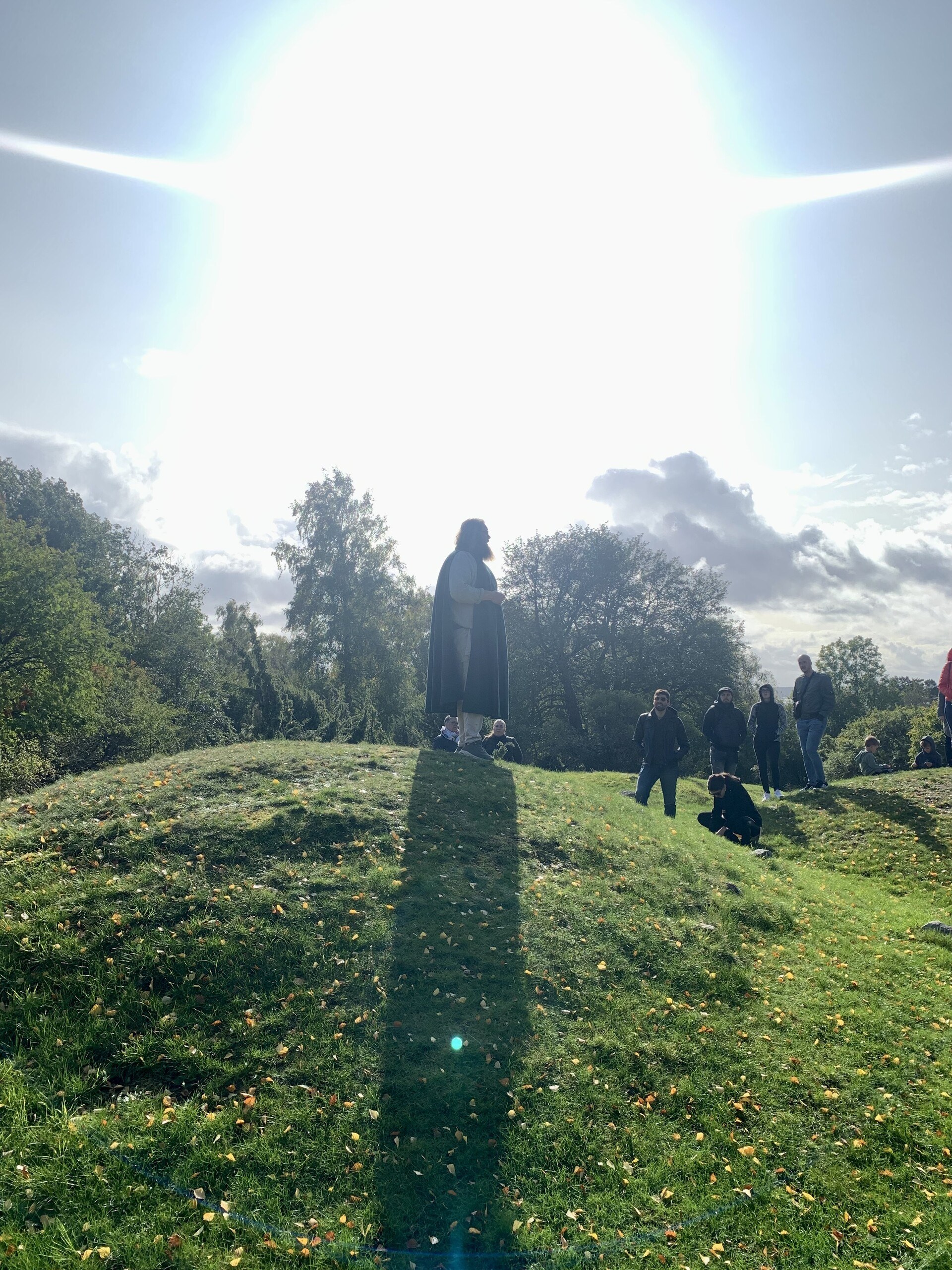A man standing on a burial mound with the sun shining down on him from behind in dramatic fashion