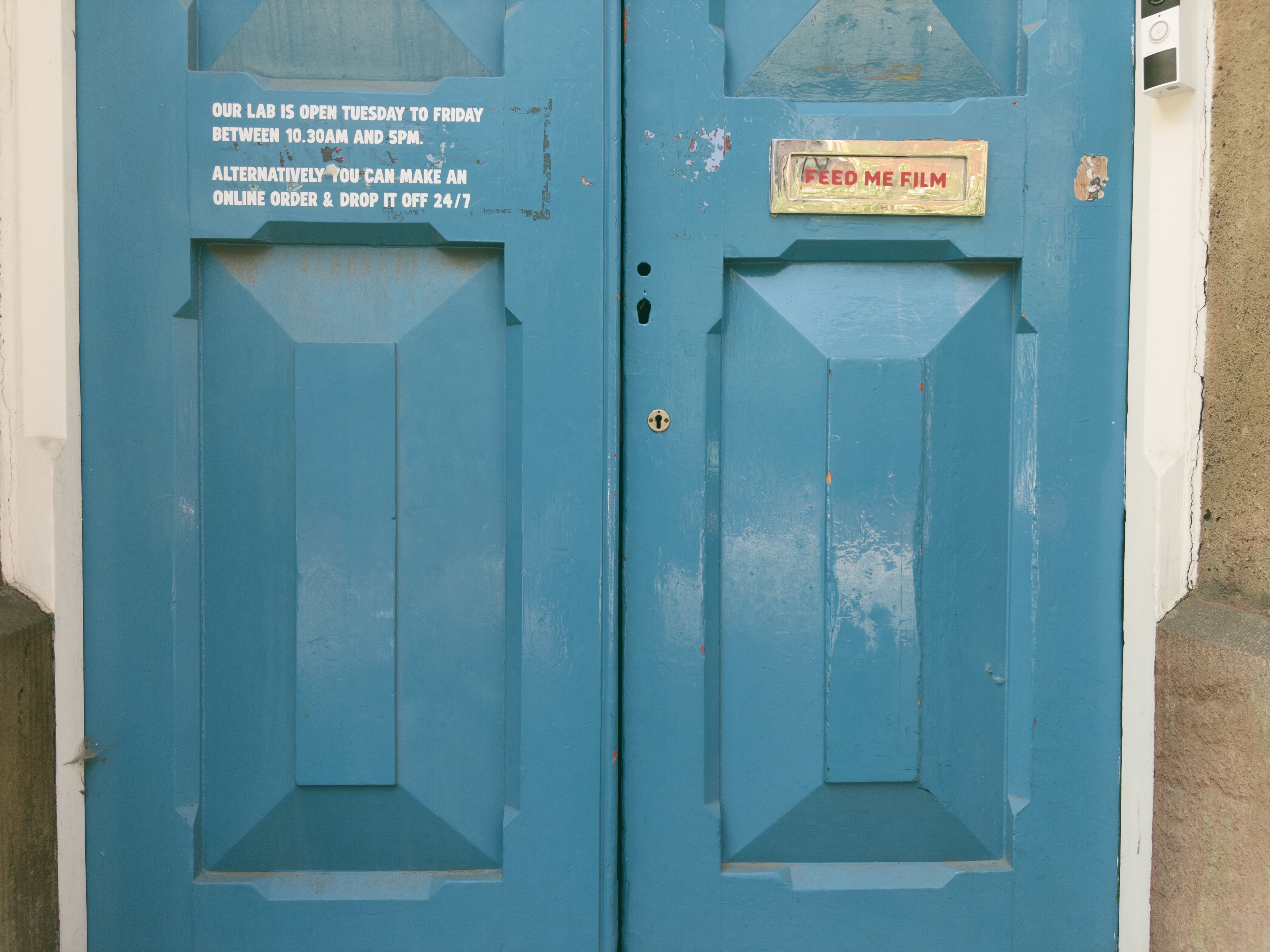 A blue pair of doors with opening times printed directly on one side, and a letterbox reading "feed me film" on the other