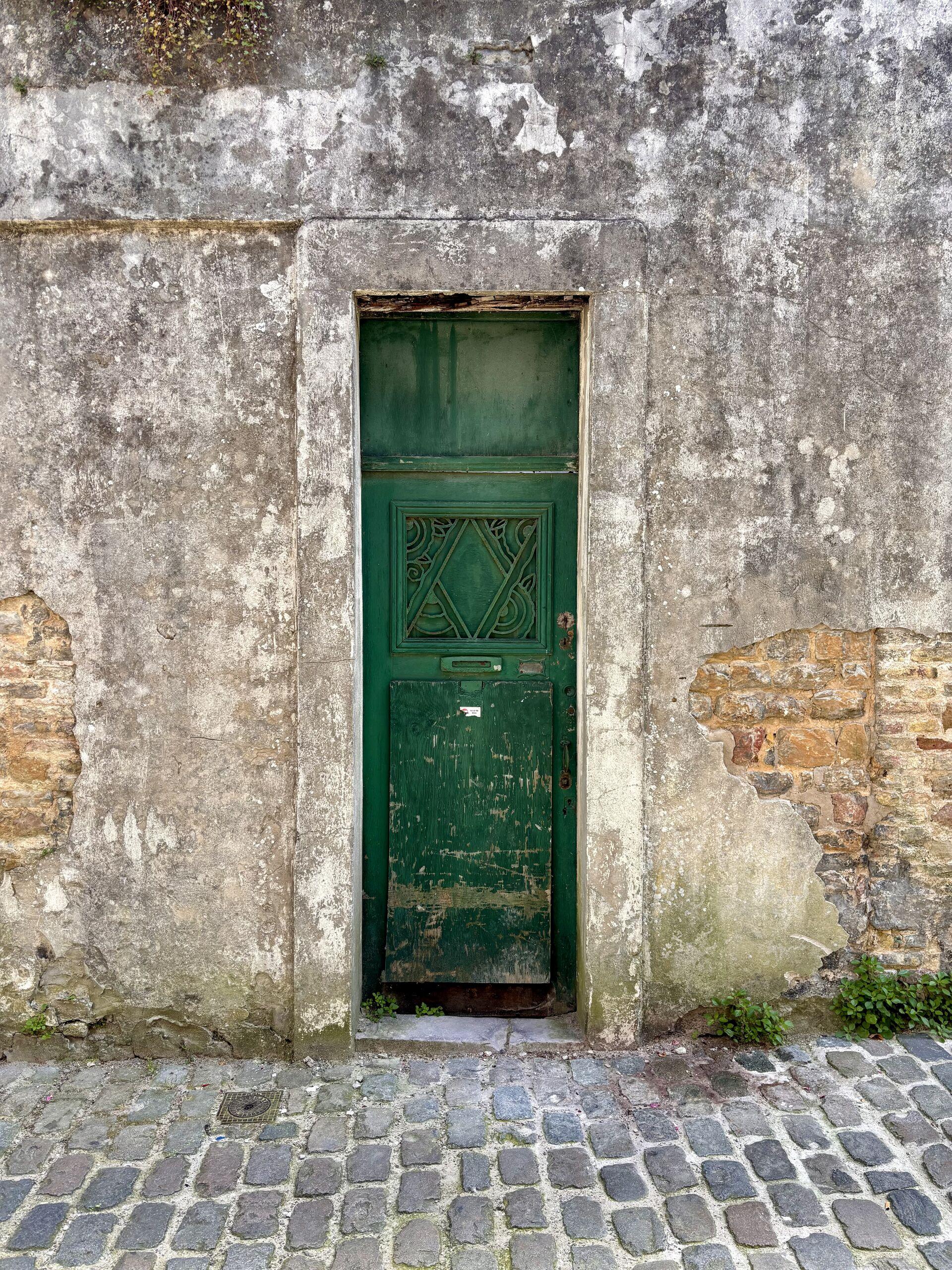 A green door set in a plastered wall, the plaster long since crumbling