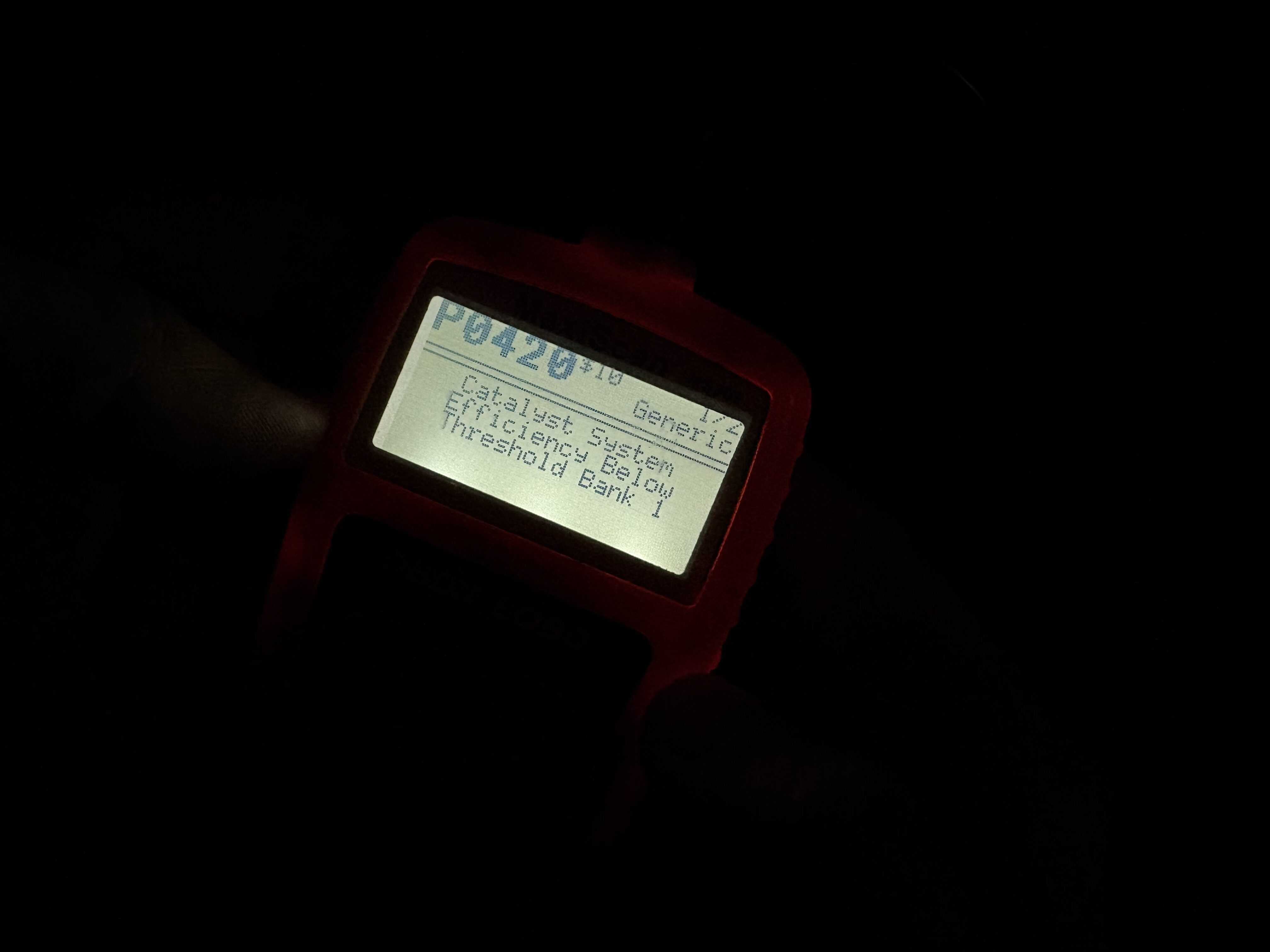 The screen of an OBDII reader in the dark, reading "Catalyst System Efficiency Below Threshold Bank 1"