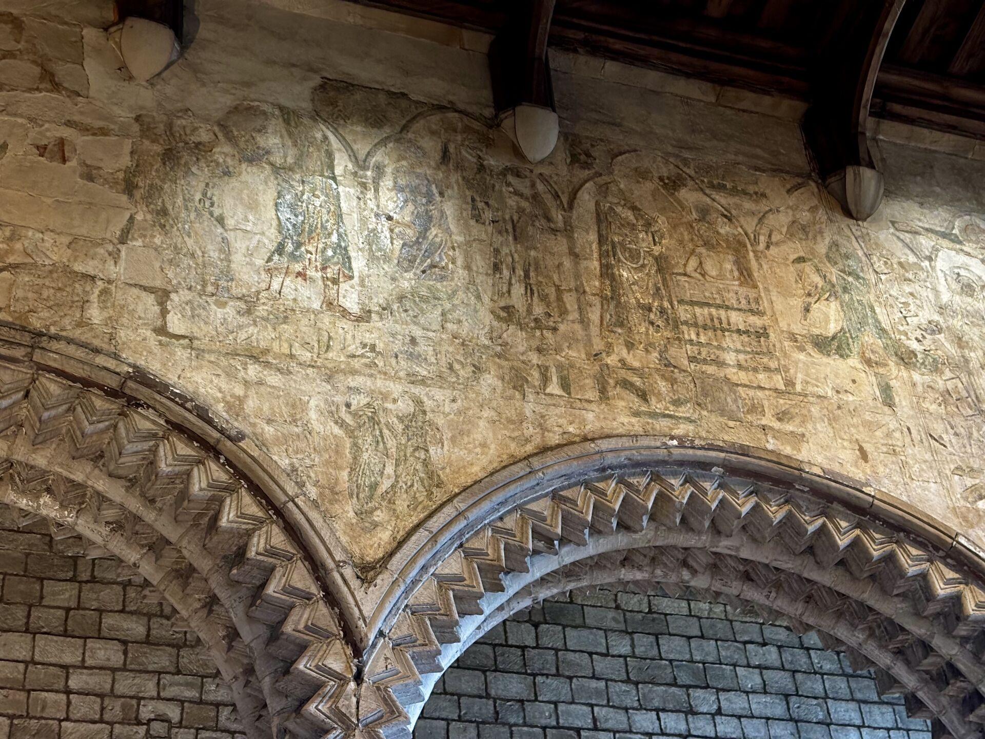 Faded medieval paintwork on a stone wall above some zigzag arches