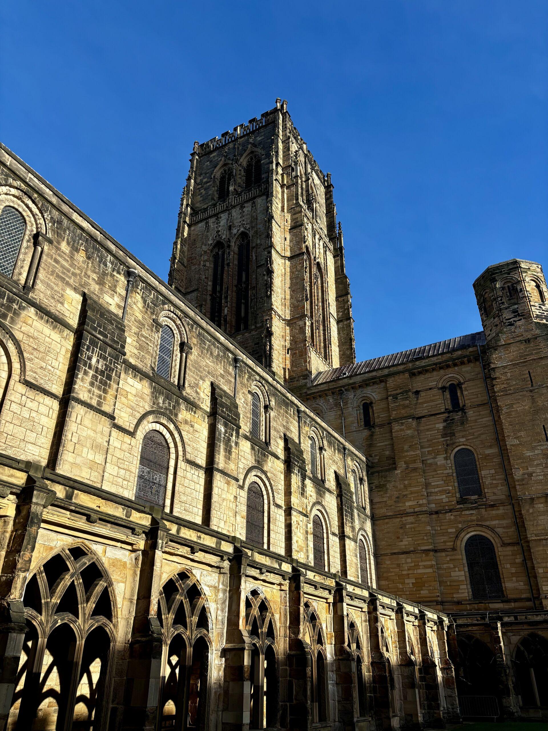 A tall gothic cathedral tower rising above the yellow stonework of Durham Cathedral cloister