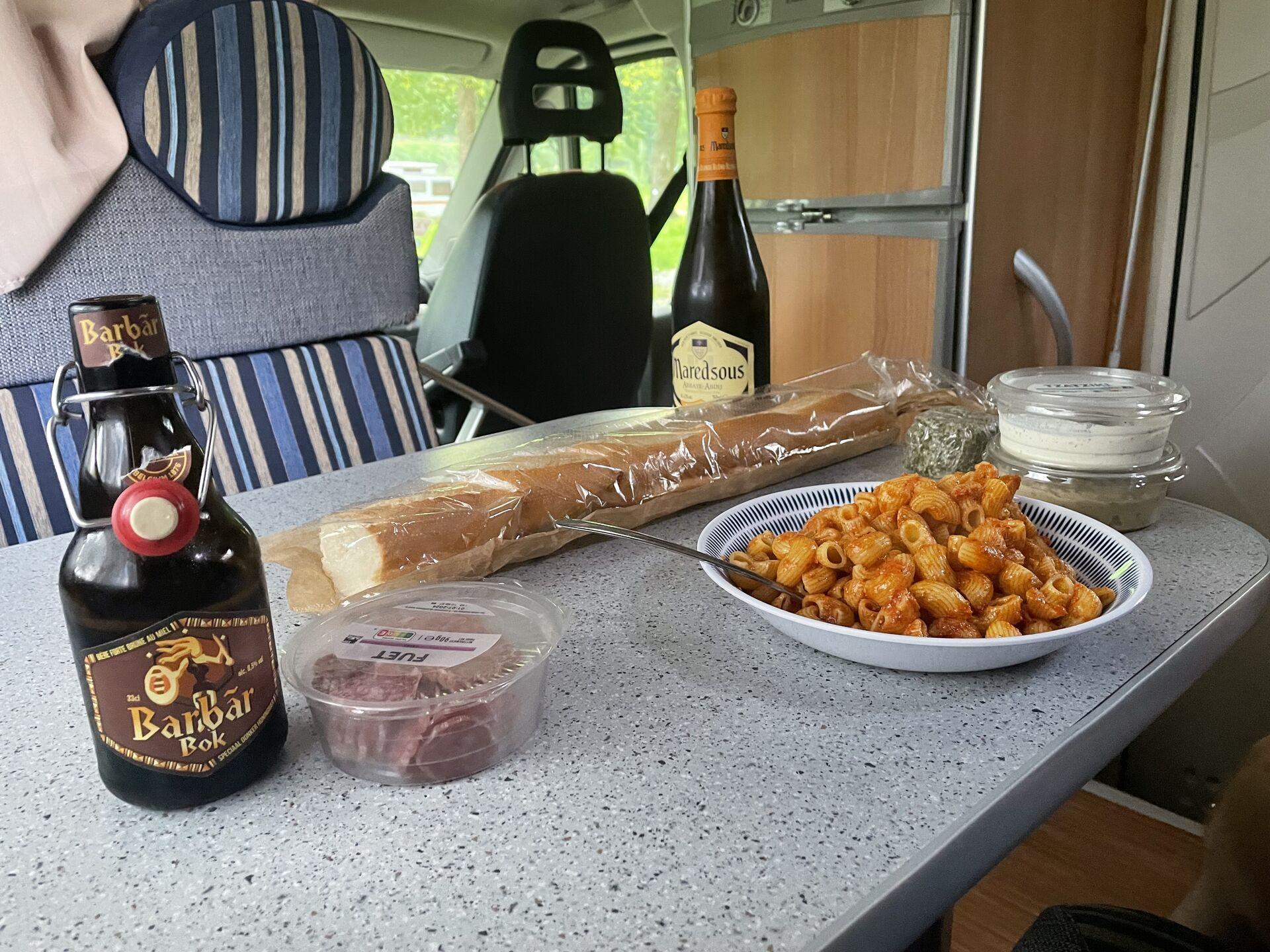 Pasta, salami, bread, cheese, dips, and beer on the table of a campervan