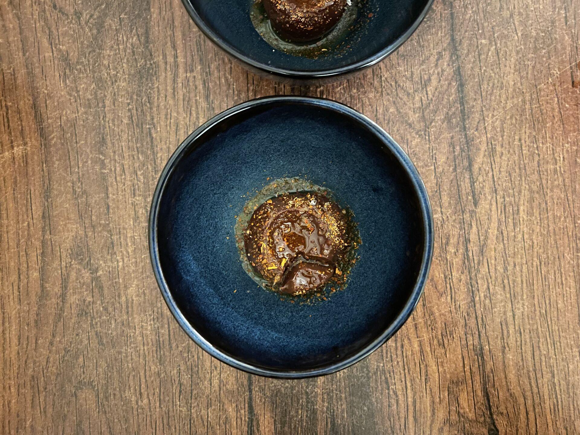 A blue bowl with a pat of whipped chocolate sitting in a drizzle of oil, with gold leaf on top - a fancy dessert