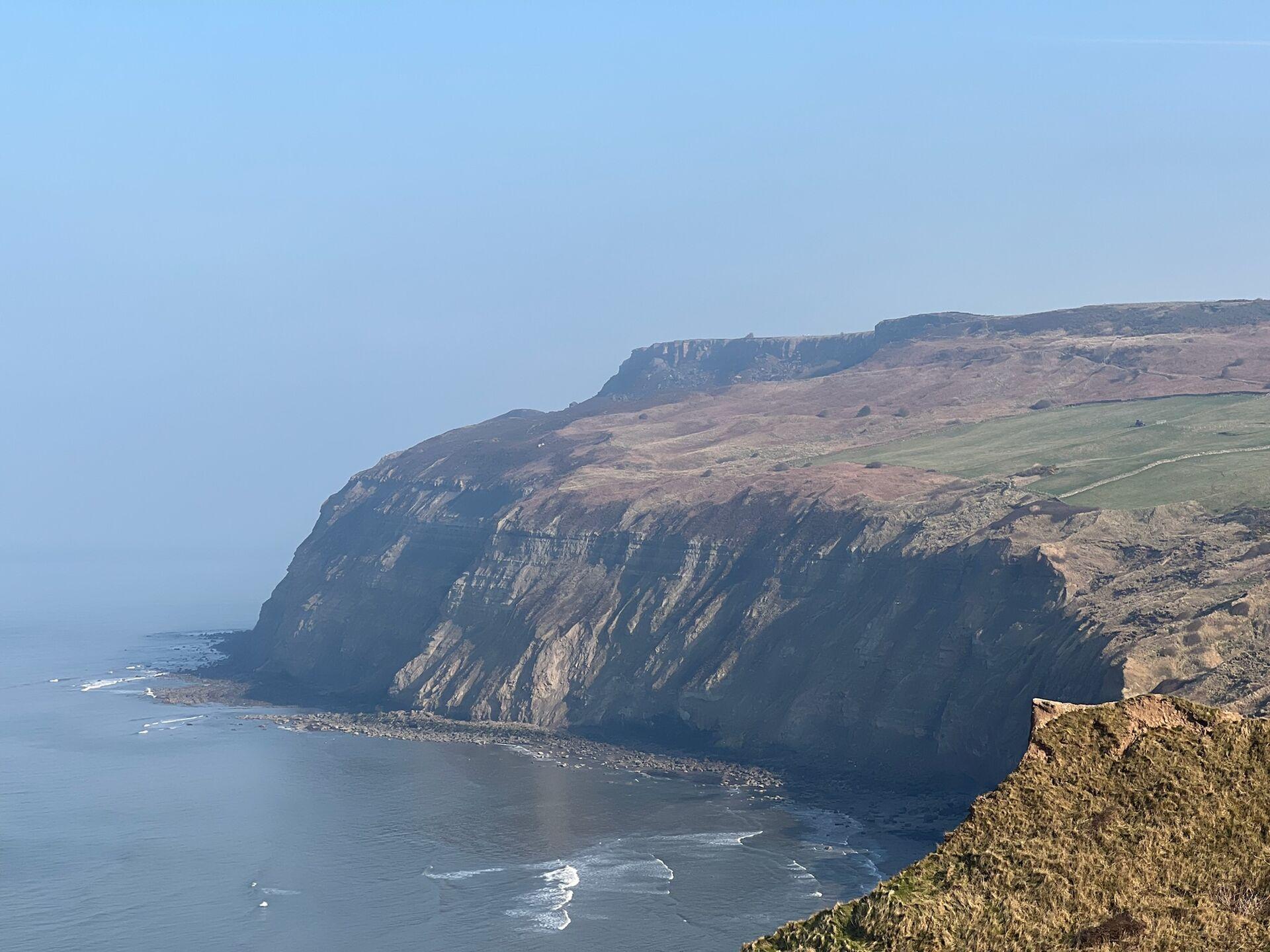 Cliffs overlooking the ocean with a distant view of grassy and rocky terrain on top.