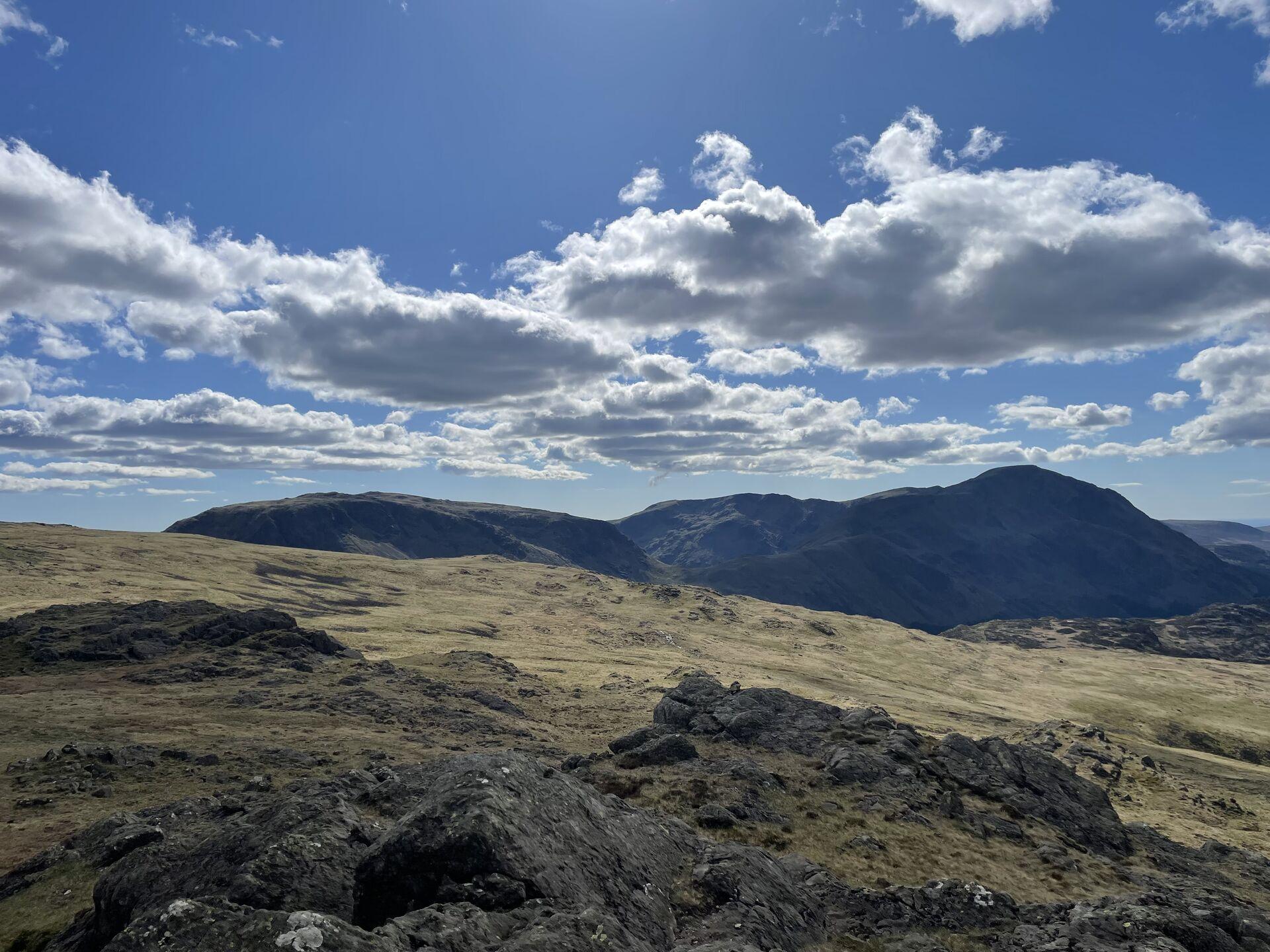 A view across to a craggy massif with a grassy landscape dotted with rocks in the foreground