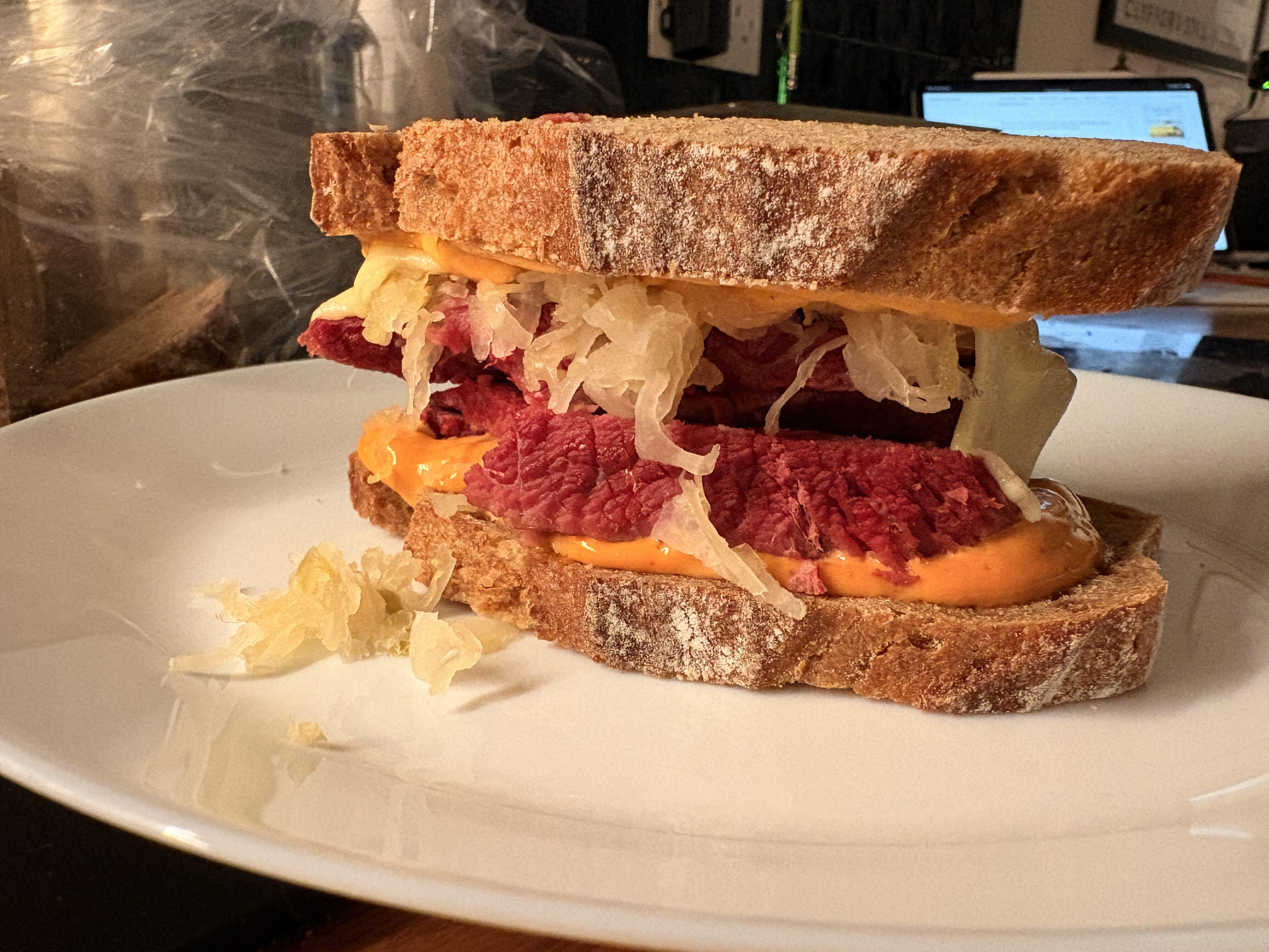 A close up of a corned beef sandwich, with sauerkraut and russian sauce, between two loaves of rye bread. I think they call this a Reuben