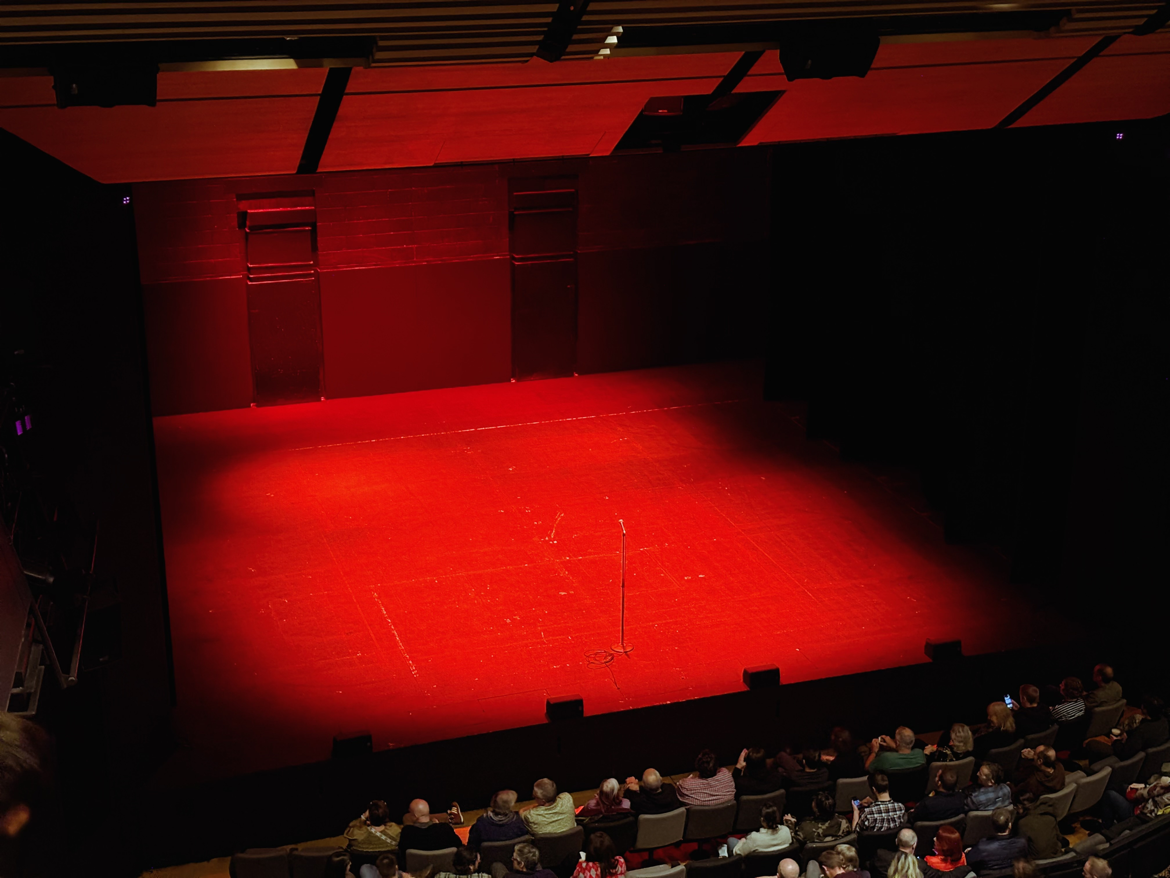 An empty red stage seen from a seat in the nosebleeds. The stage is undressed and there's no one on it. The first three rows of seats are visible at bottom right.