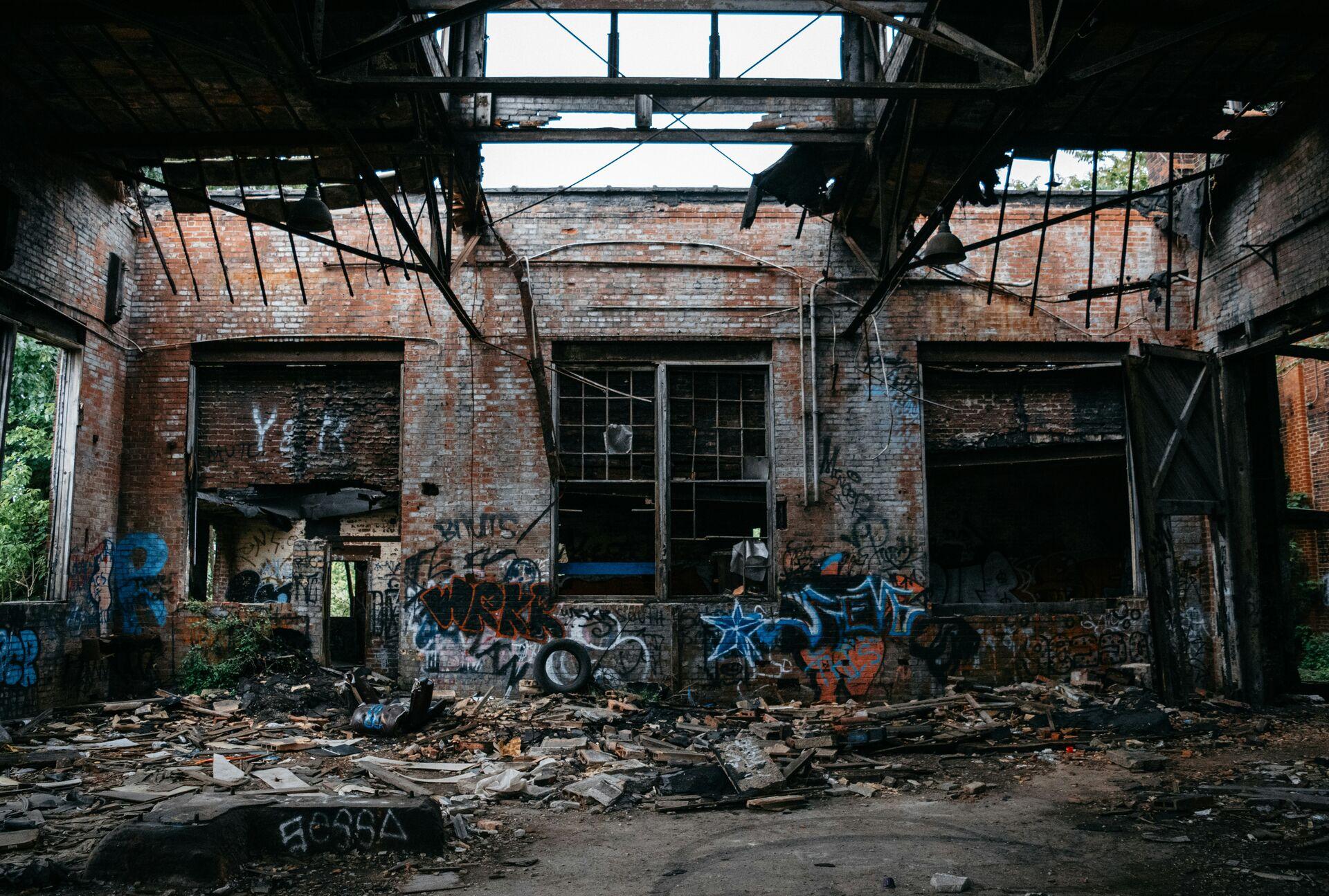 The dilapidated interior of a brick industrial building with graffiti on the walls and rubble on the ground