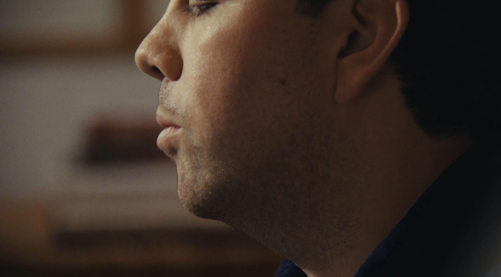 A closeup profile shot of a guy talking, with the background totally out of focus, soft lighting, lots of film grain
