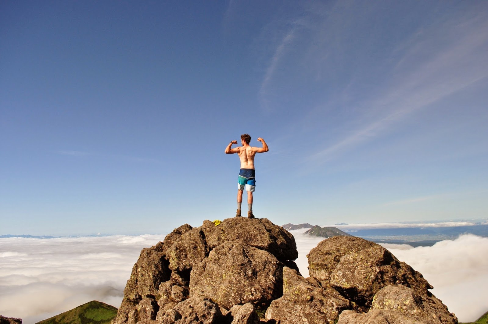 Flexing my arms and back, standing on the summit of the mountain, facing away from the camera, looking very dramatic