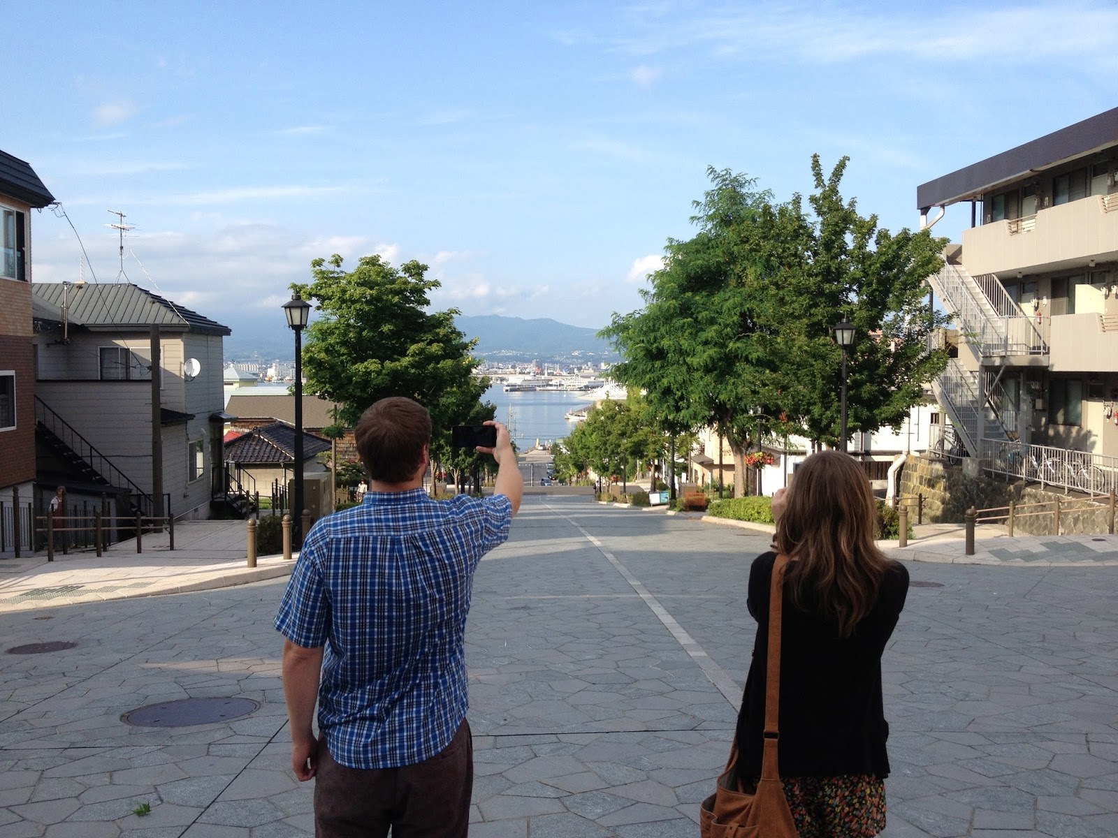 Oliver and Emma standing at the top of a long sloping San Francisco-style road, taking pictures looking down towards the sea