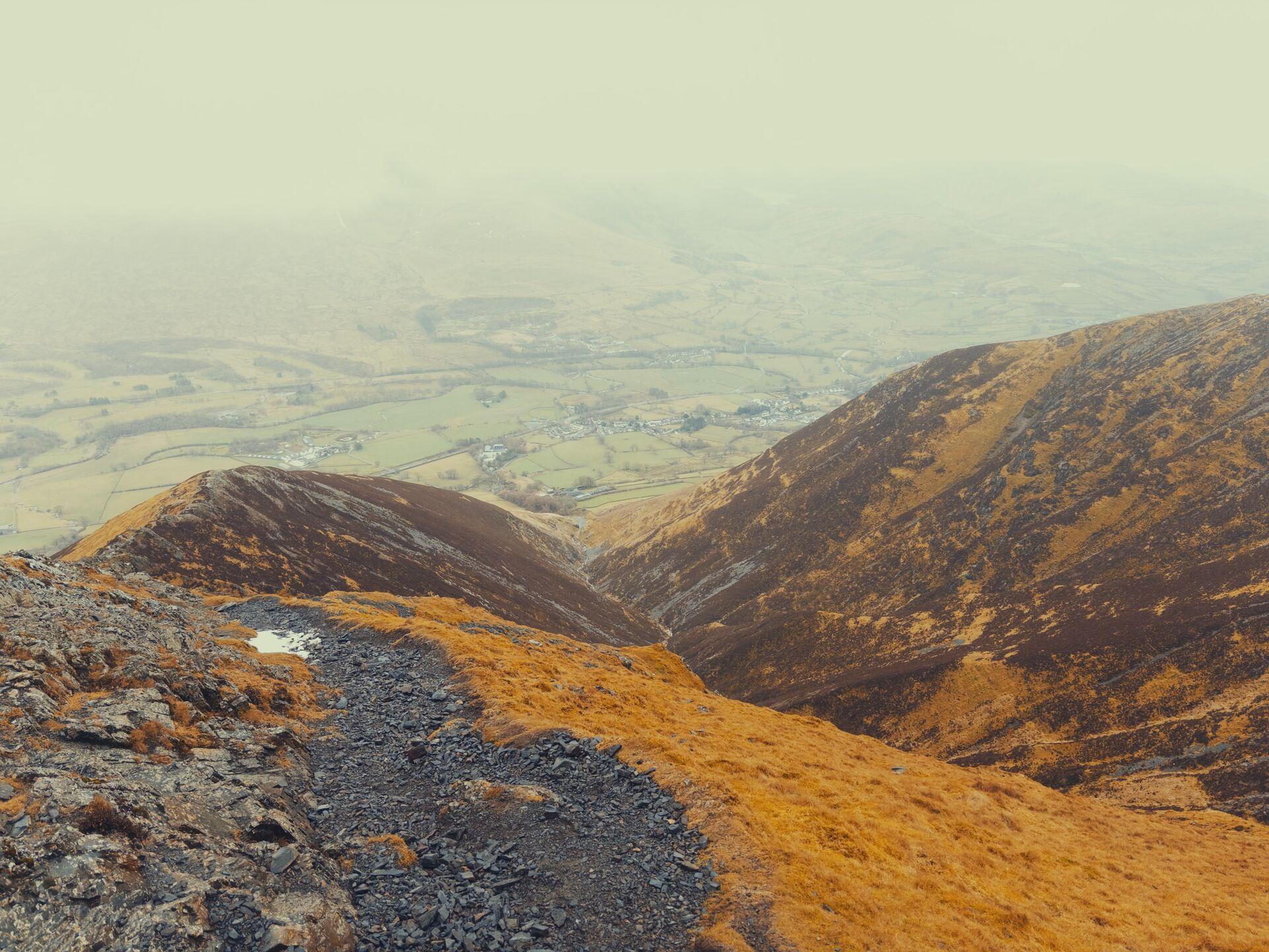 Looking down a craggy ridgeline at the pastureland spotted with trees below
