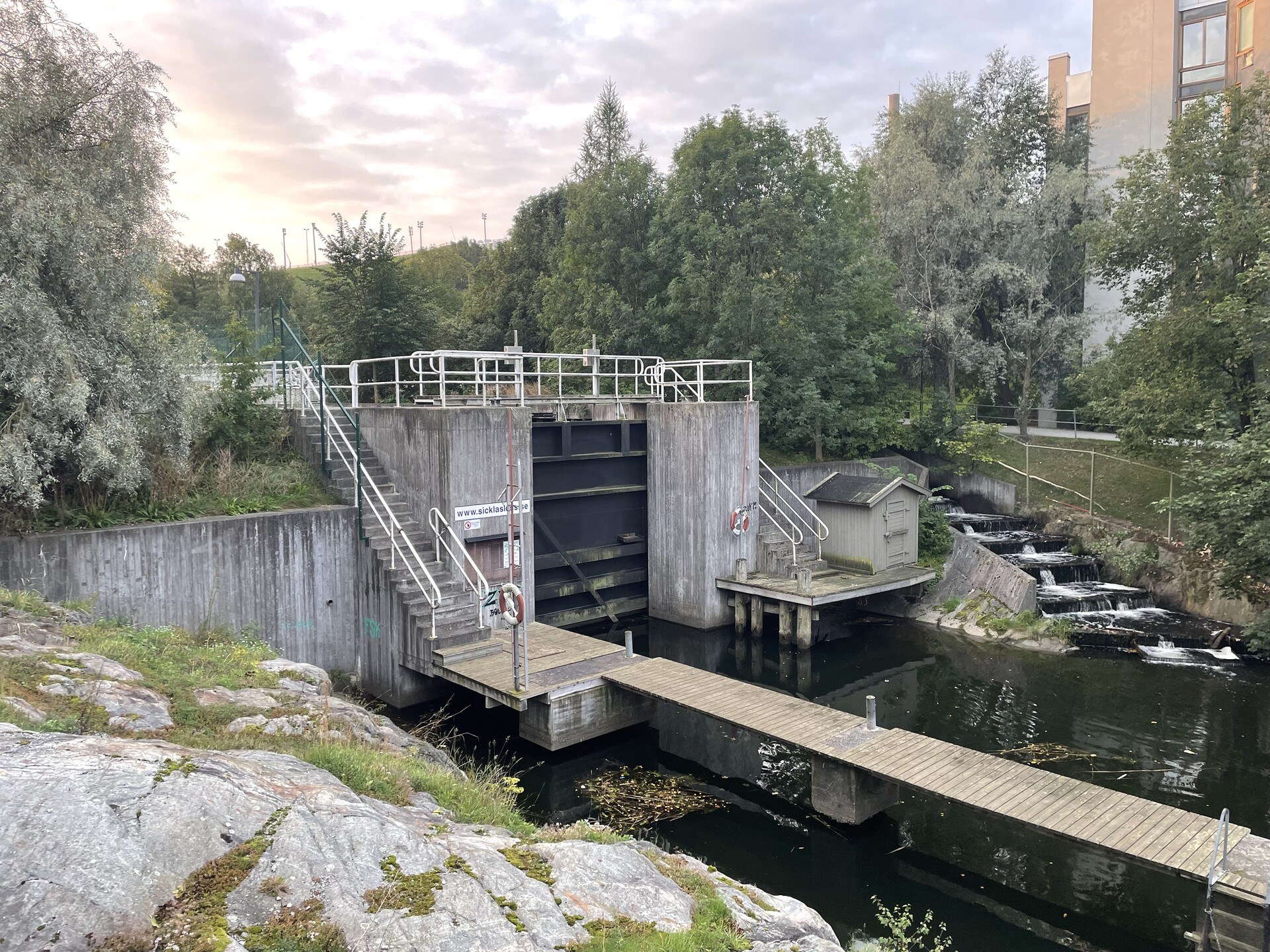 A lock on a canal, with trees and rock on either side, and an apartment building abutting a terraced slipway just to the right