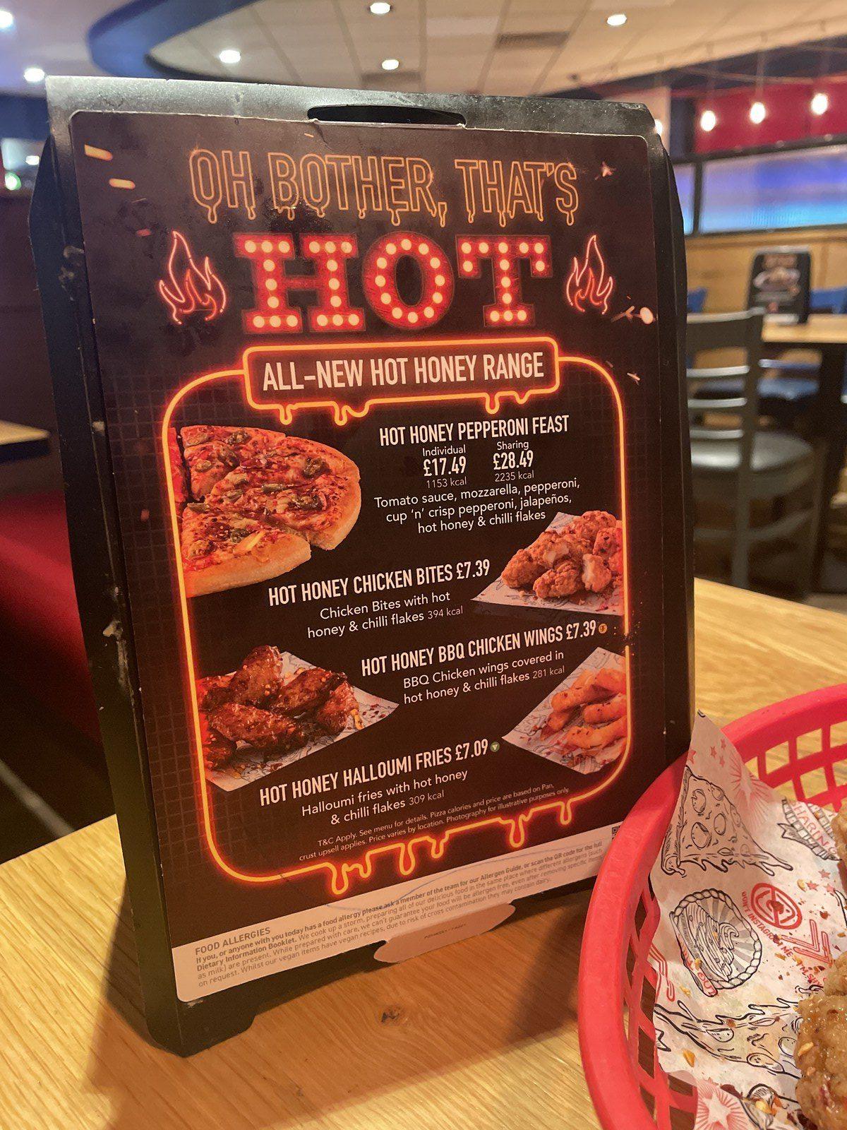 A placard advertising hot honey pizzas, wings, and halloumi fries at Pizza Hut