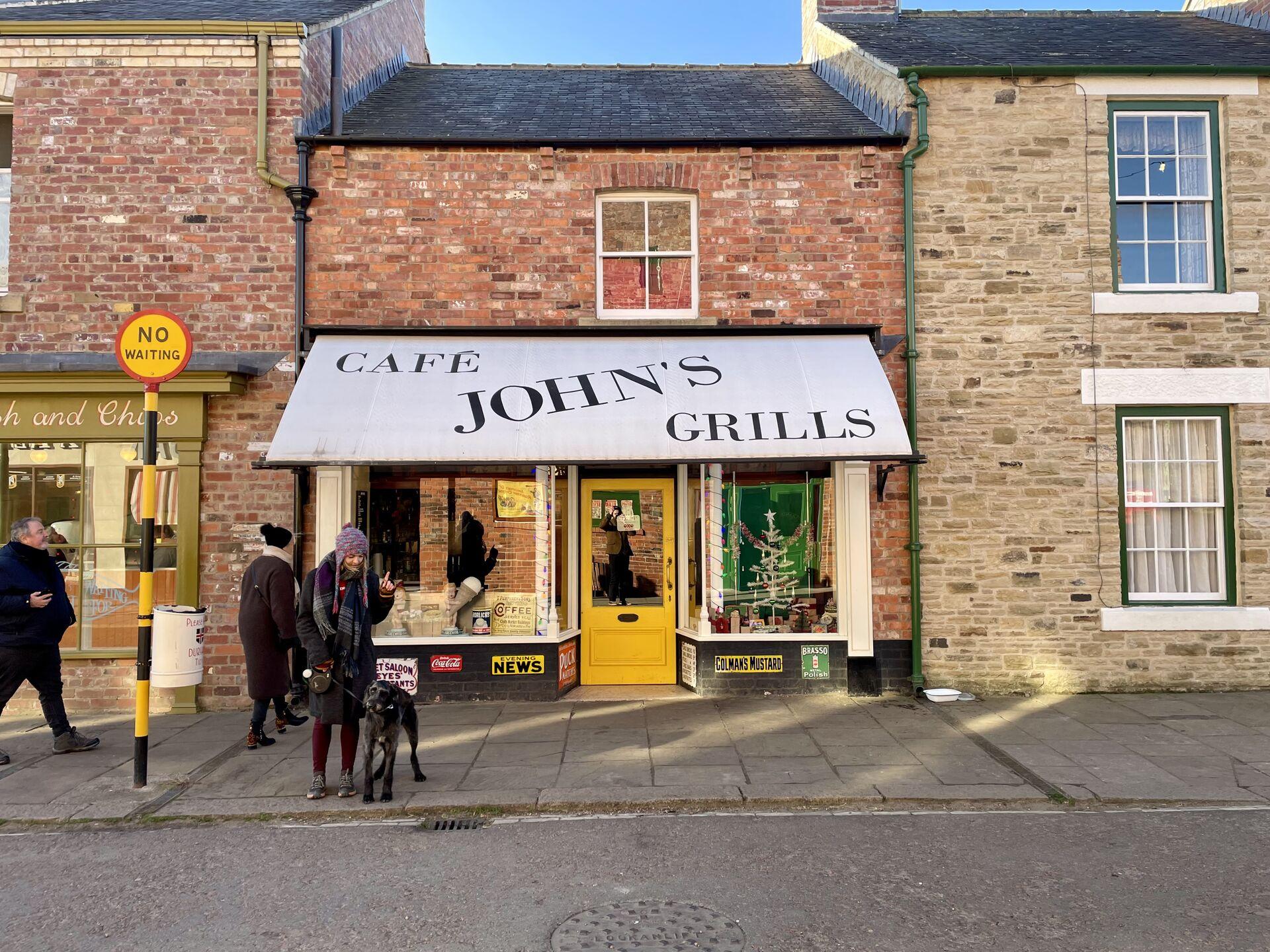 A building with a "Cafe John's Grills" awning, wedged between two other row houses of different heights