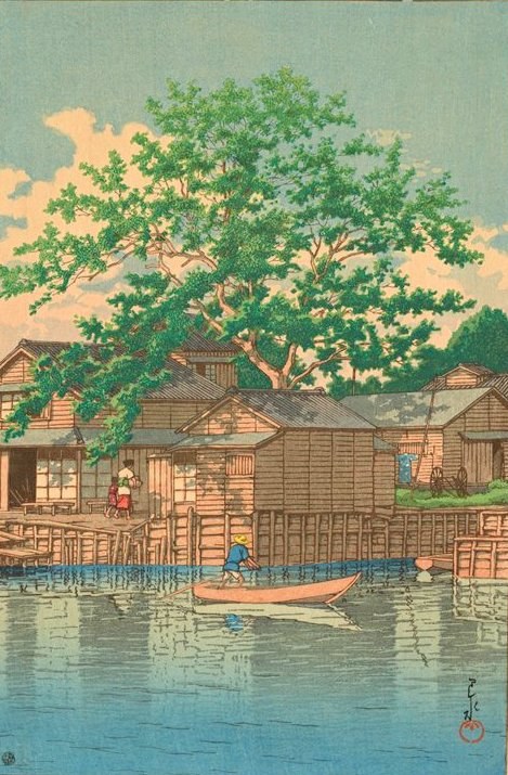 Woodblock print of Japanese houses on the waterside, with a couple of boatmen in the water in the foreground and a big green tree in the background