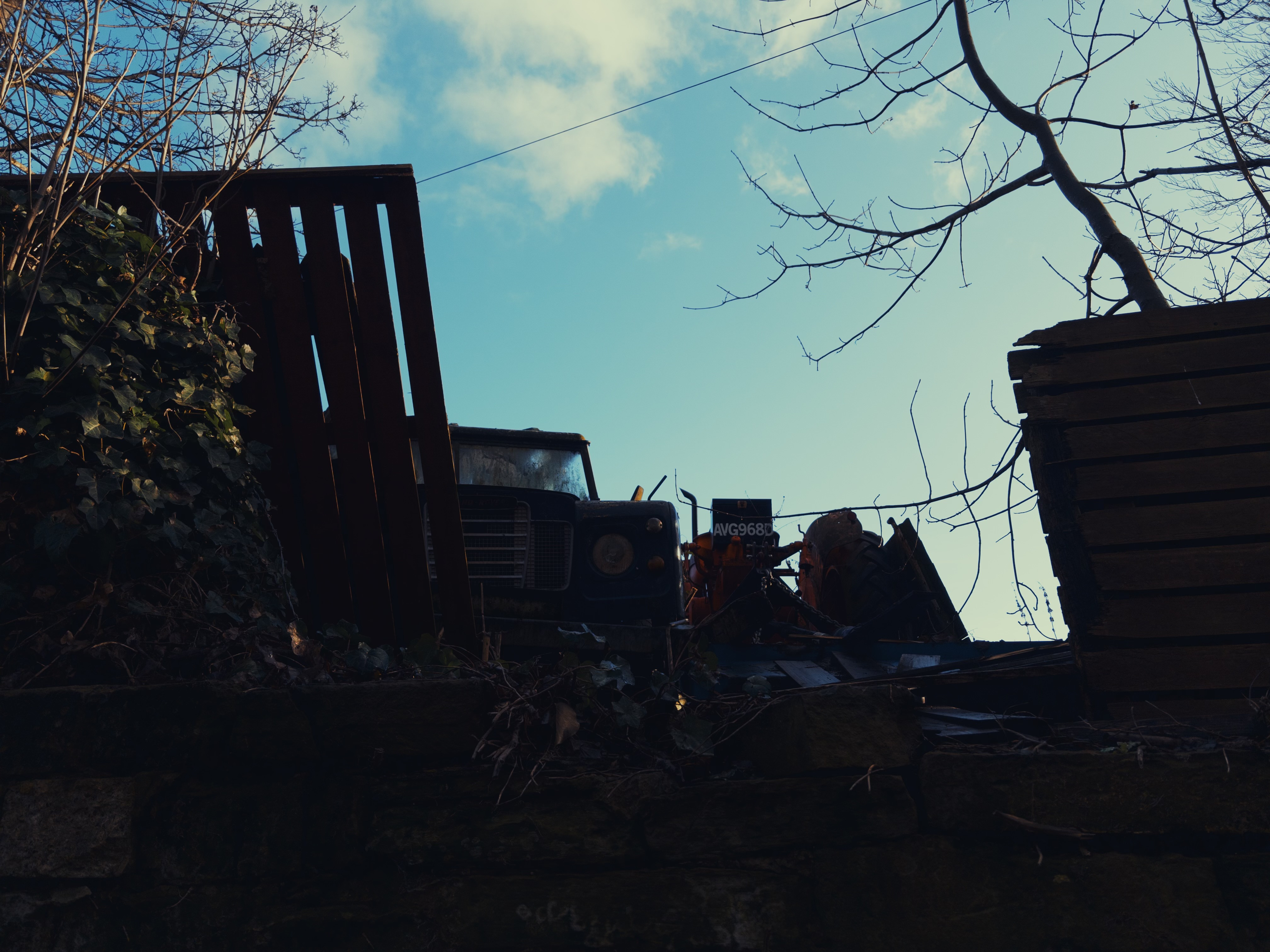 Looking up at a Land Rover Defender sitting in pieces in a yard, partially obscured by a fence.