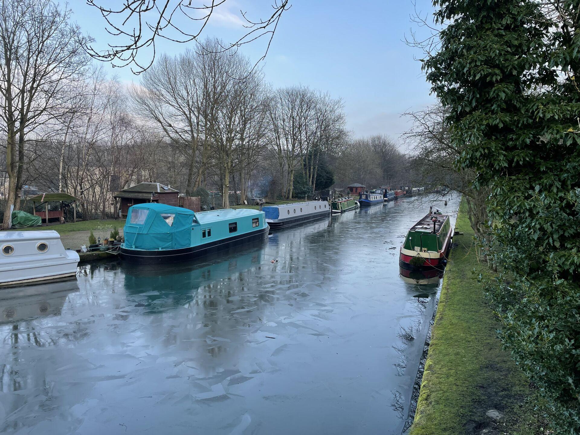 Narrowboats lined up along the Leeds & Liverpool Canal, with a thin layer of ice on the surface of the water