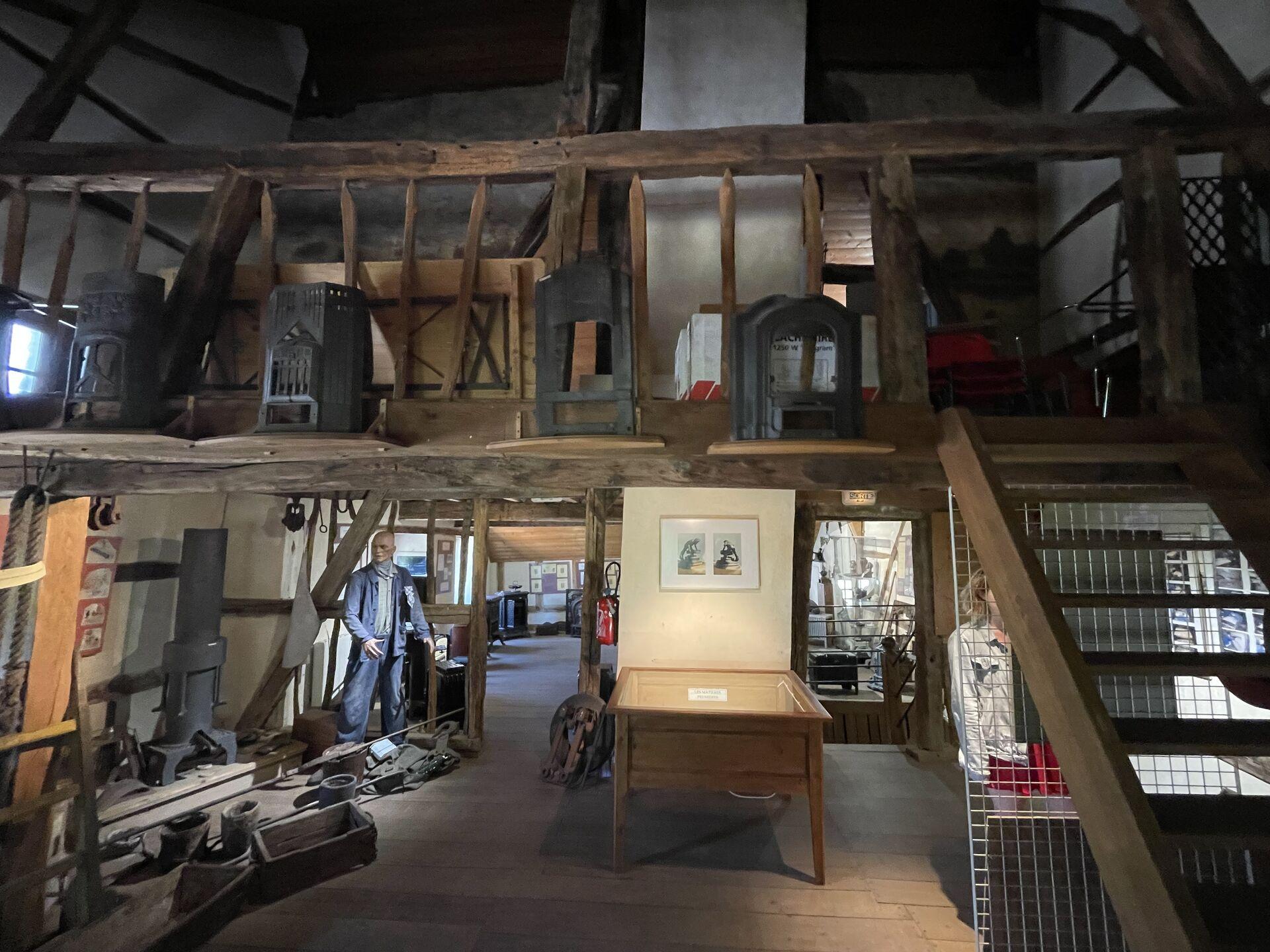 A cluttered wooden interior with assorted farming implements and cast iron stoves split across a main level and a raised, closed-off, loft