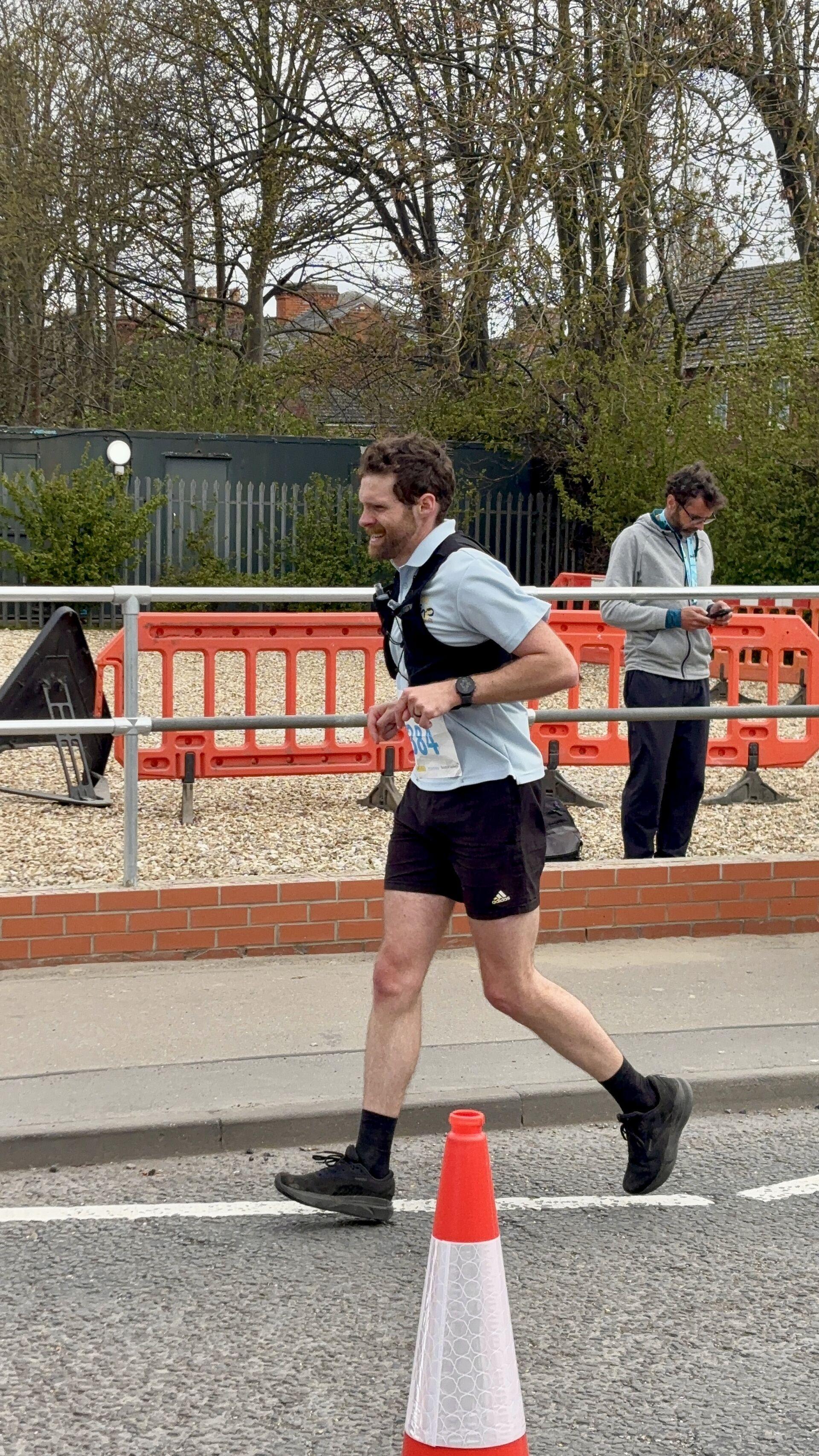 A man in a running vest finishing a marathon; he's evidently in a lot of pain
