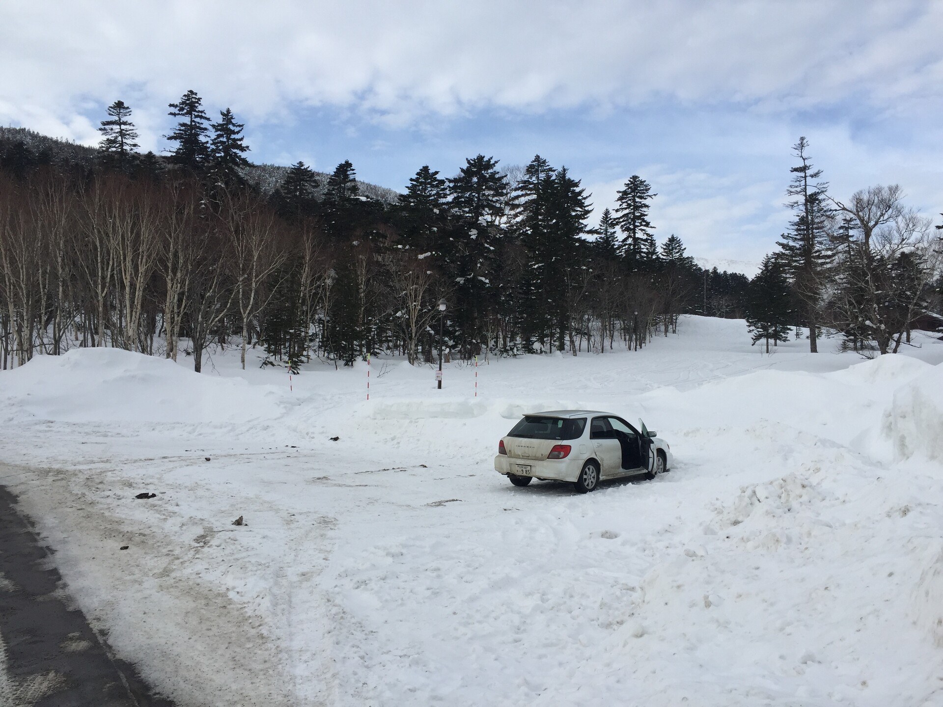 My Subaru Impreza parked in a big ploughed-out car park on the side of the road, snow all round and a forested slope beyond