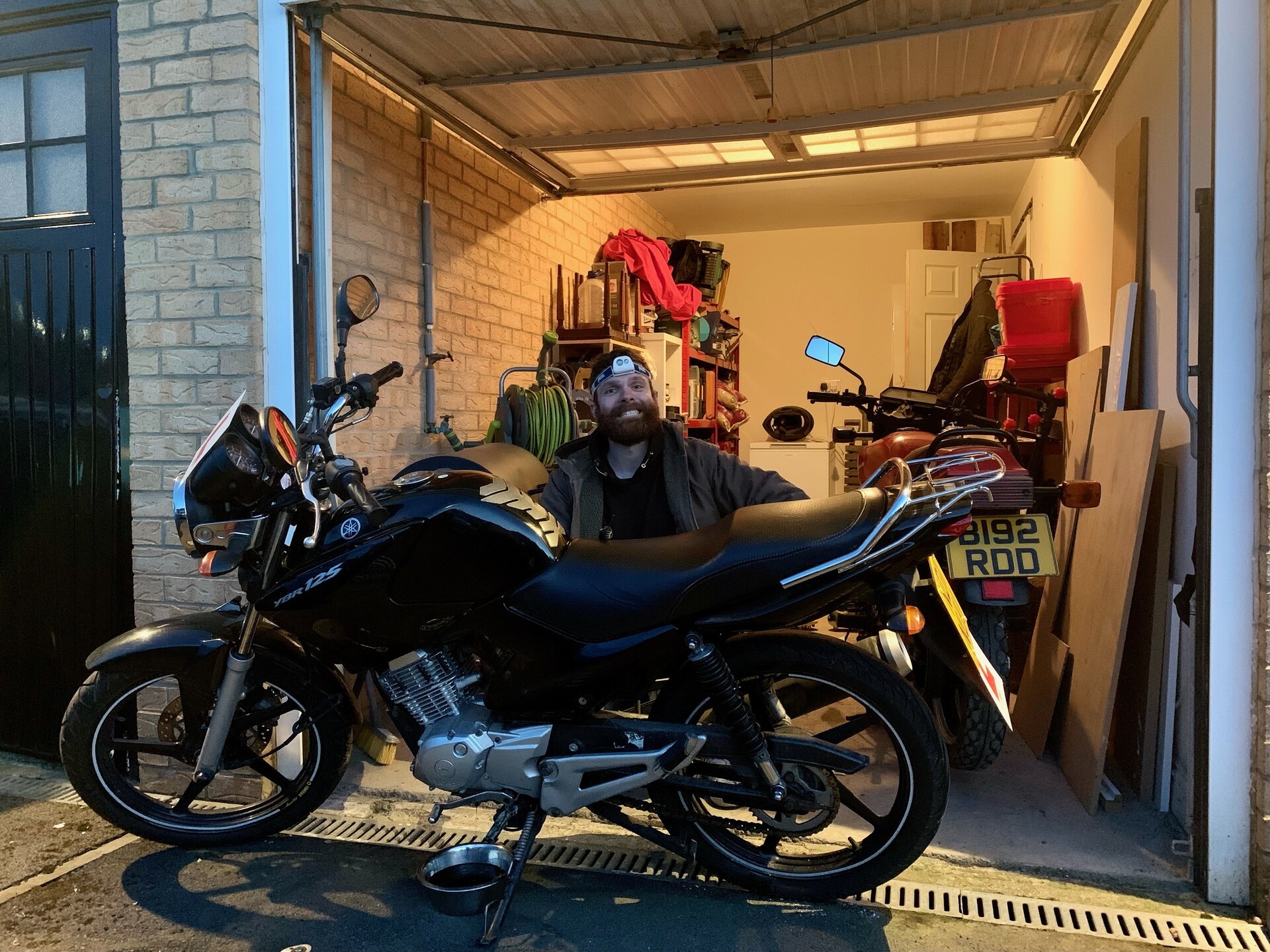 Me, smiling, kneeling behind a Yamaha YBR in my driveway, clearly in the middle of changing the oil