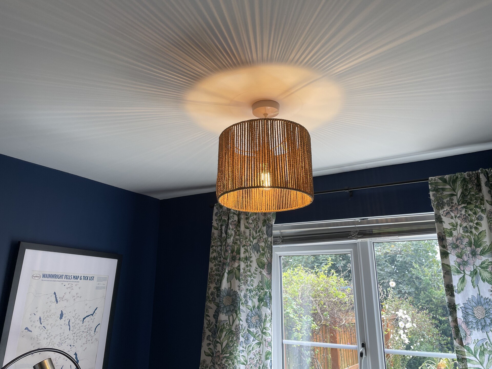 A hanging ceiling light, illuminated from within & casting shadows on the ceiling around it
