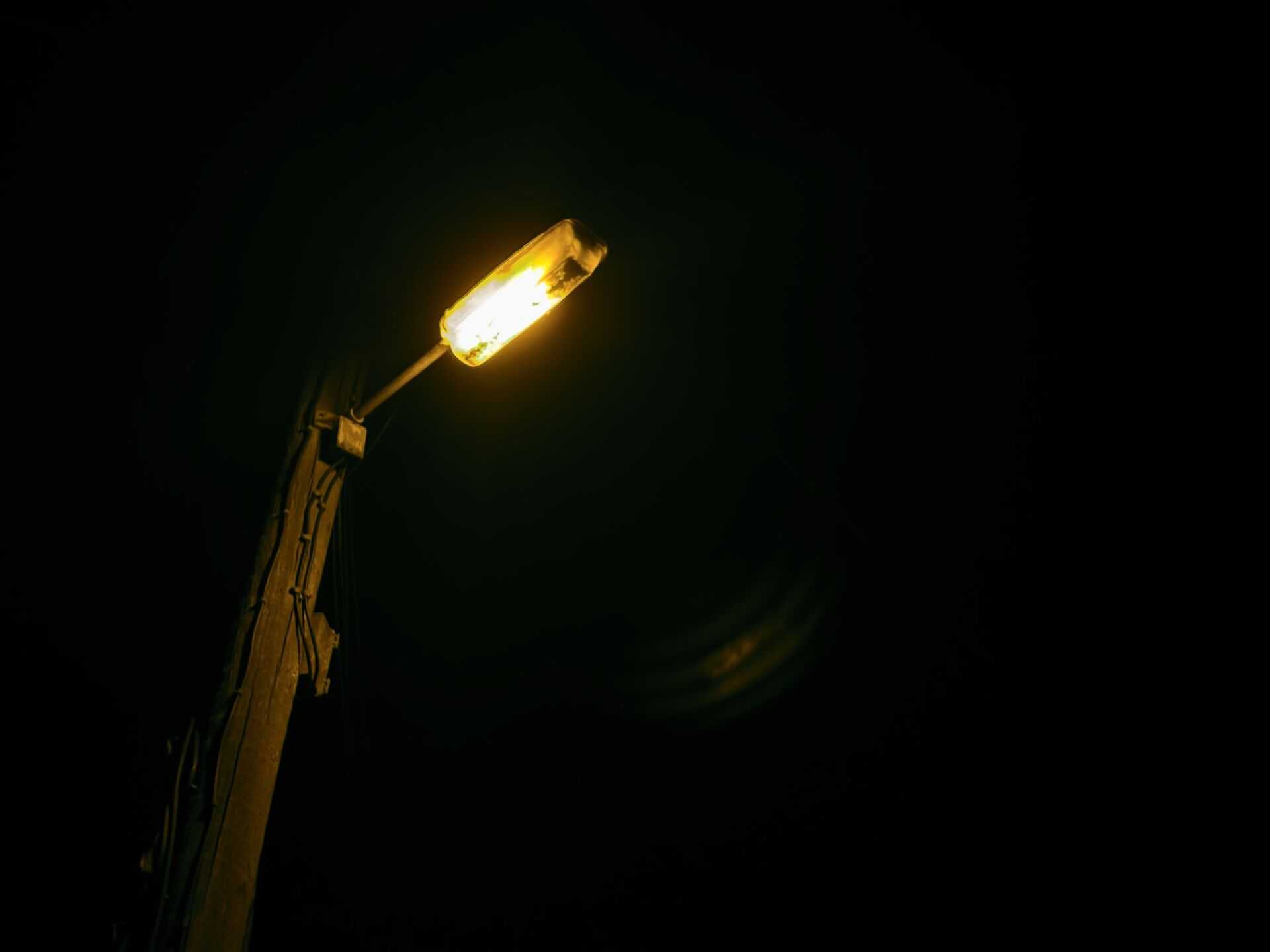 A glowing street lamp on a wooden pole stands out against a completely black night sky.