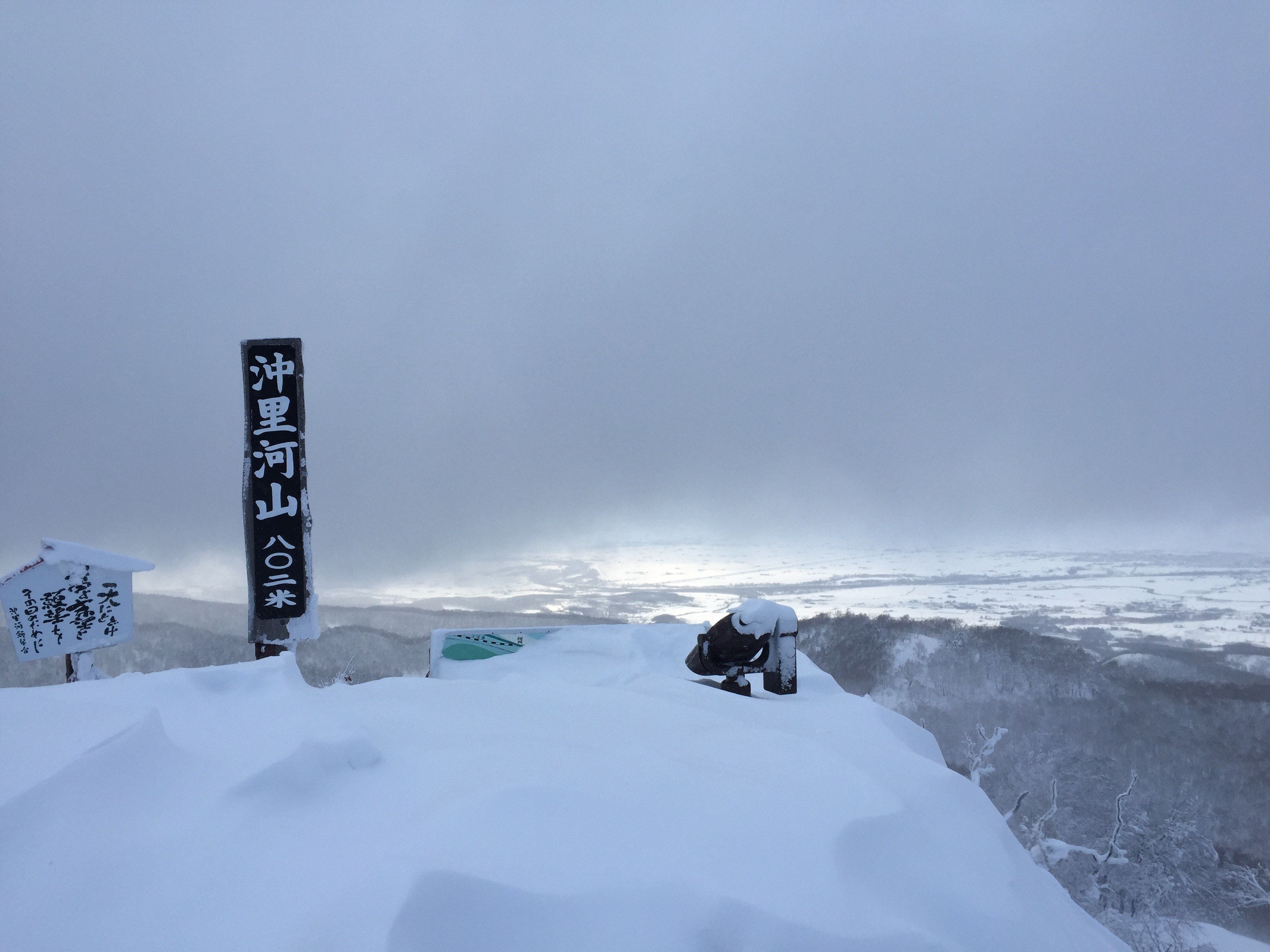 A cloudy view from the summit of Okirika-yama, with almost everything but the summit marker covered in windswept snow