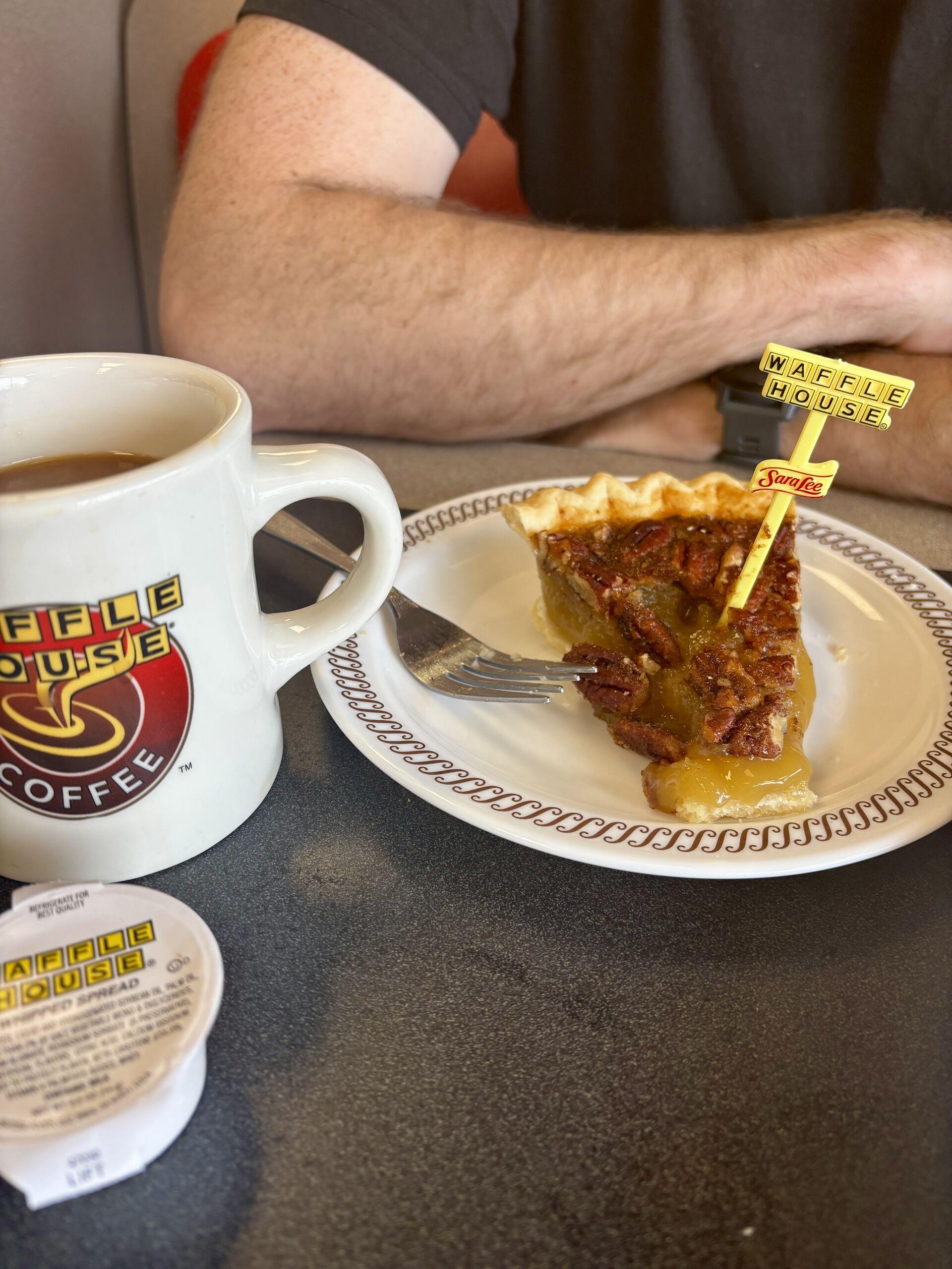 A cup of coffee and a slice of pecan pie on a plate, with a little waffle house sign on a skewer