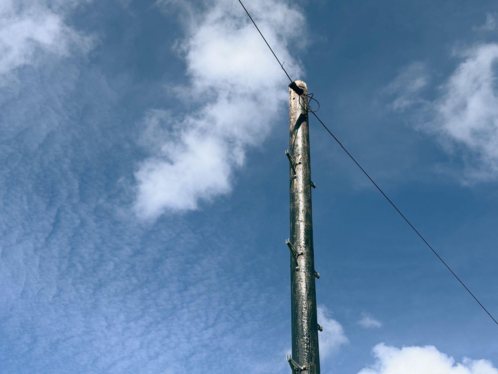 A wooden utility pole with a single wire stretching diagonally across a blue sky with scattered clouds, shot from a low upward angle.