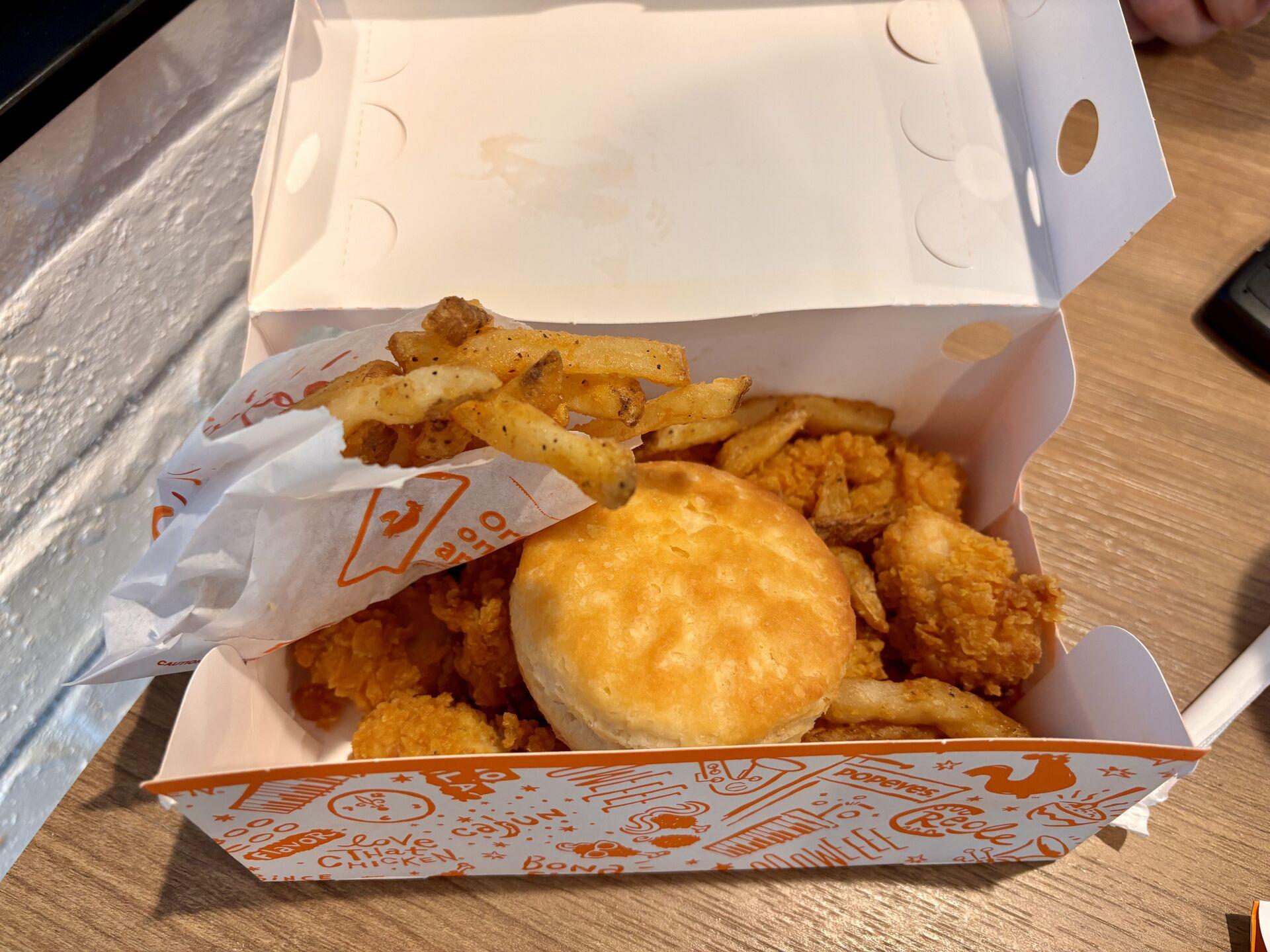 A paper box of buttermilk chicken nuggets, topped with a biscuit and a small paper bag of fries