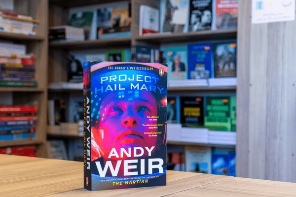 Project Hail Mary standing on end on a table in front of a bookshelf of other books