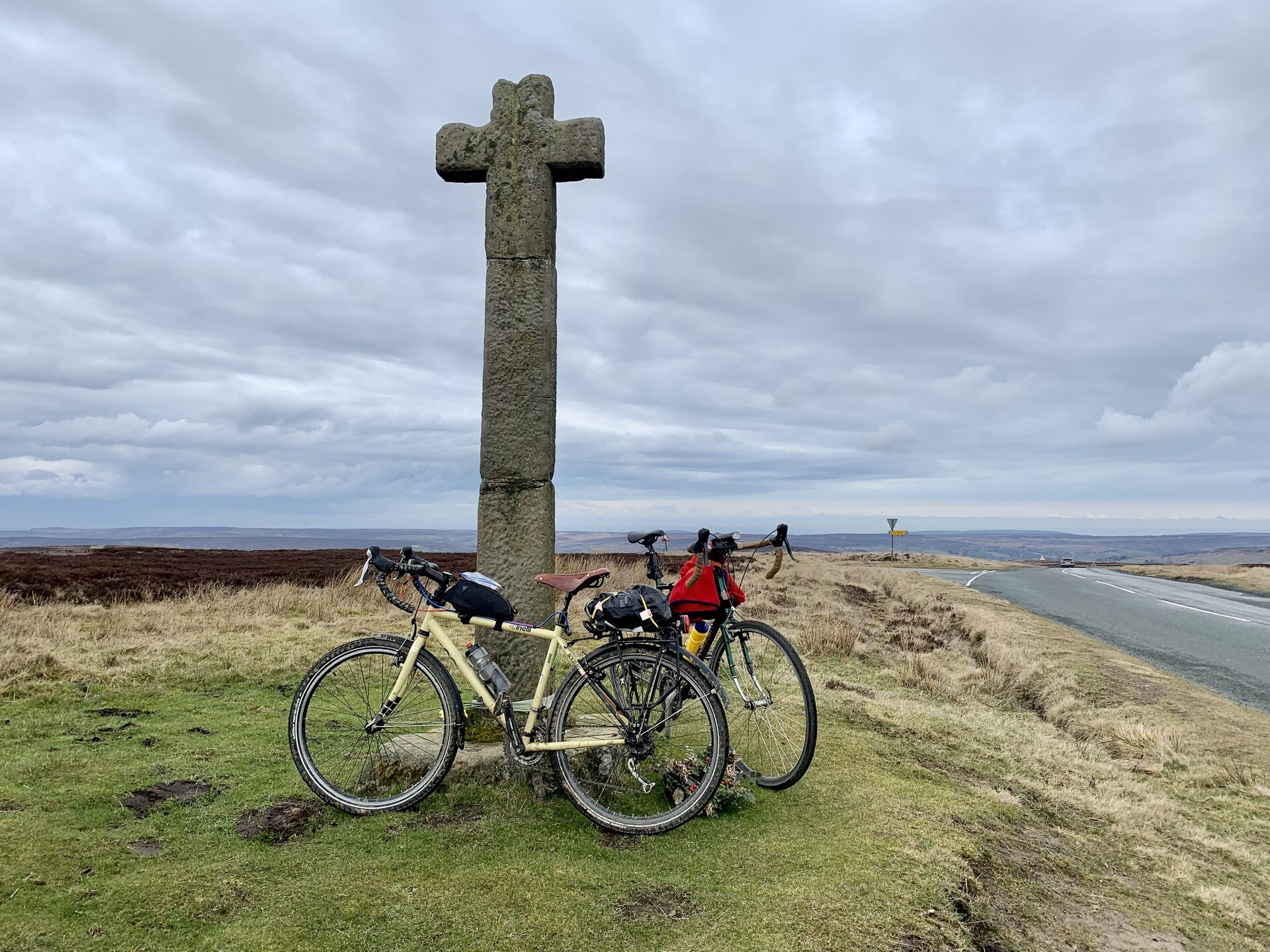 A couple of bikes leaned up against a stone cross near a road in the North York Moors